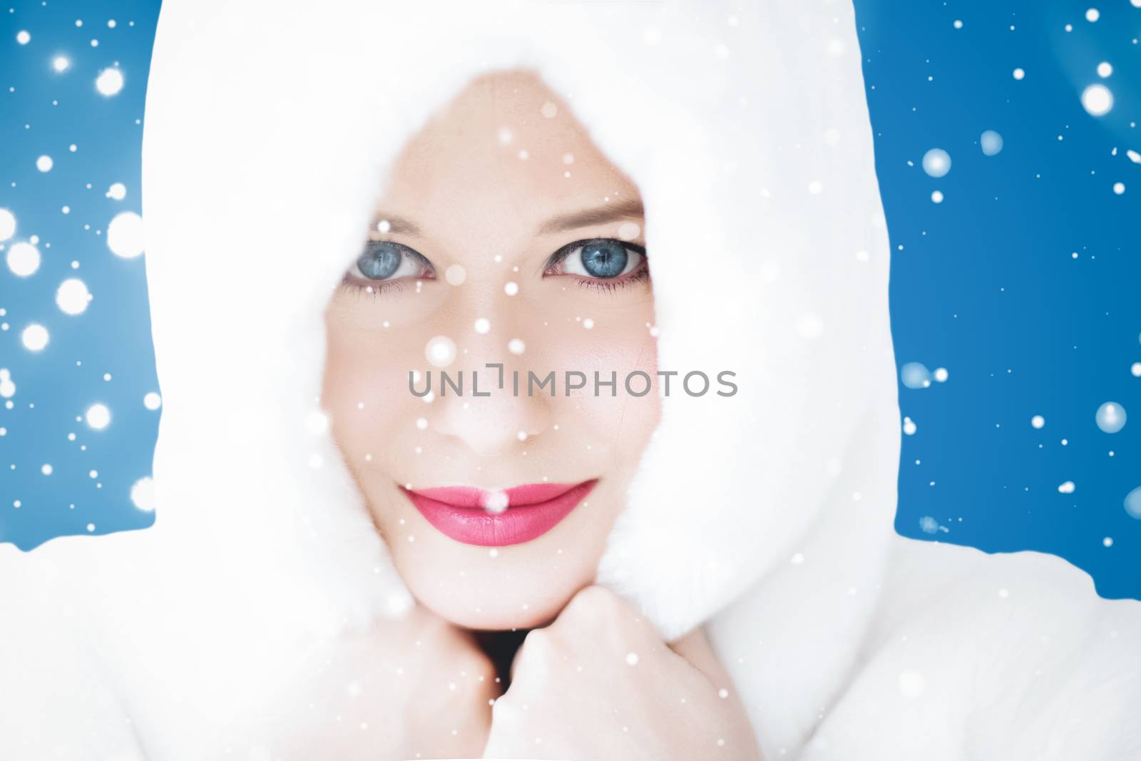 Happy Christmas and winter holiday portrait of young woman in white hooded fur coat, snow on blue background, fashion and lifestyle campaign