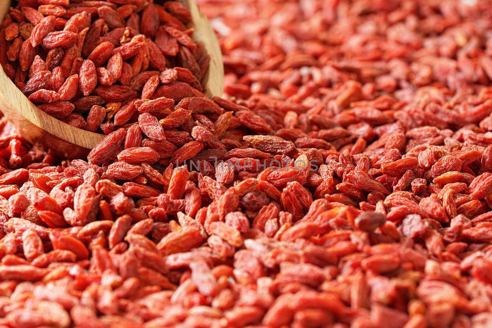 Dry goji berries in small wooden bowl, scattered on desk below by Ivanko