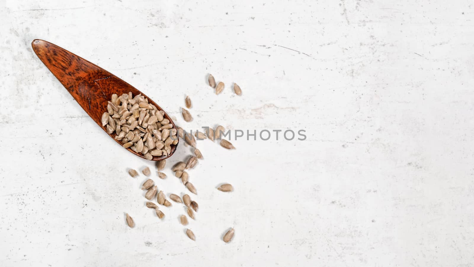 Peeled sunflower seeds in small wooden scoop, placed on white stone like board, view from above, banner space for text right side by Ivanko