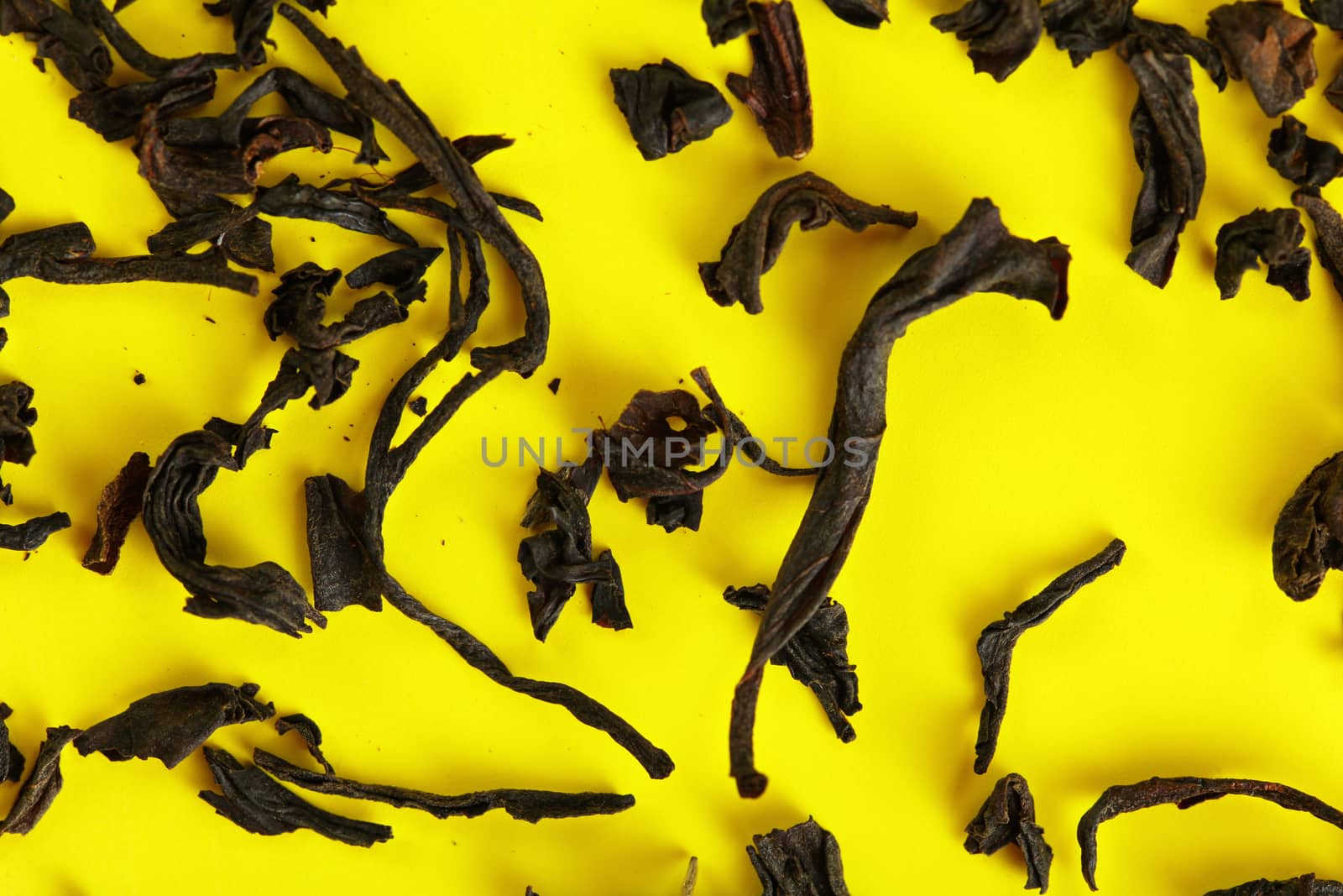 Dry black loose tea leaves on yellow board, closeup detail from above by Ivanko