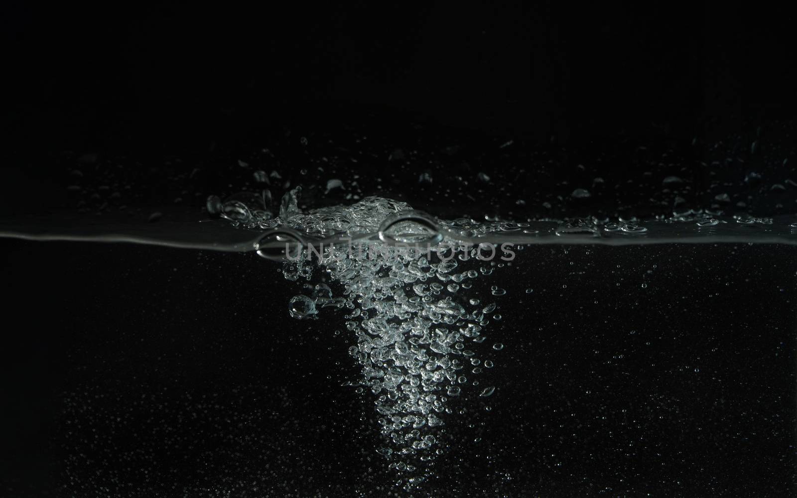 Water splashing as it's poured into aquarium tank, black background.