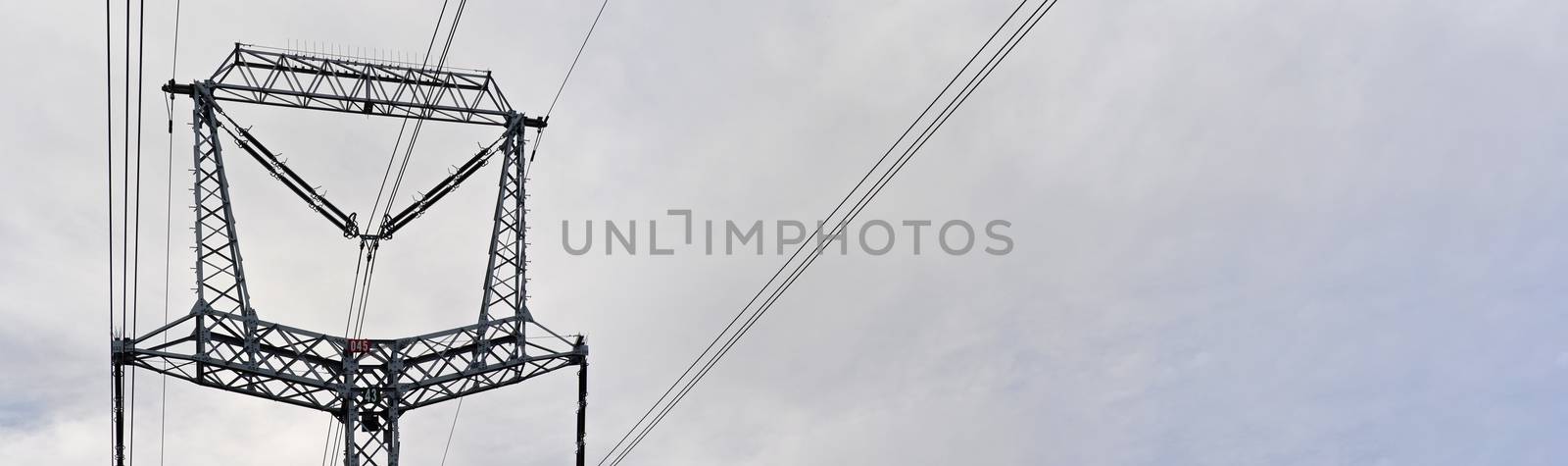 Steel power pylon construction with high voltage cables against cloudy sky. Wide banner for electric energy industry space for text on right side.