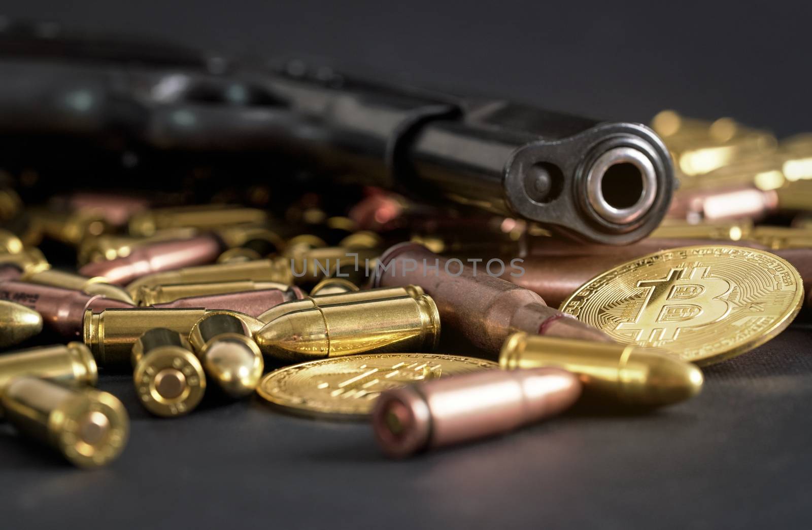 Bronze and brass gun bullets scattered on dark table, black pistol barrel, golden bitcoin coins near - illegal use of cryptocurrency to purchase weapon concept by Ivanko