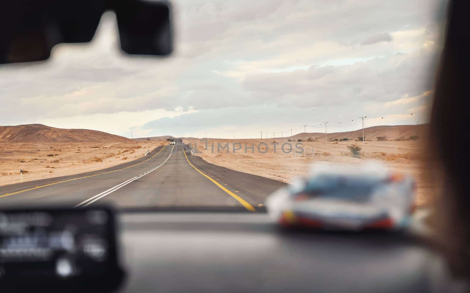 Car driving through desert landscape on overcast day, view from passenger seat, blurred dashboard foreground, roadtrip concept.