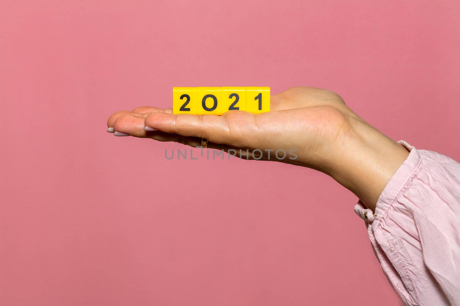Female hand holding a bunch of yellow cubes with black digits which form 2021. Pink background. Close up shot. Christmas, new years celebration season concept.