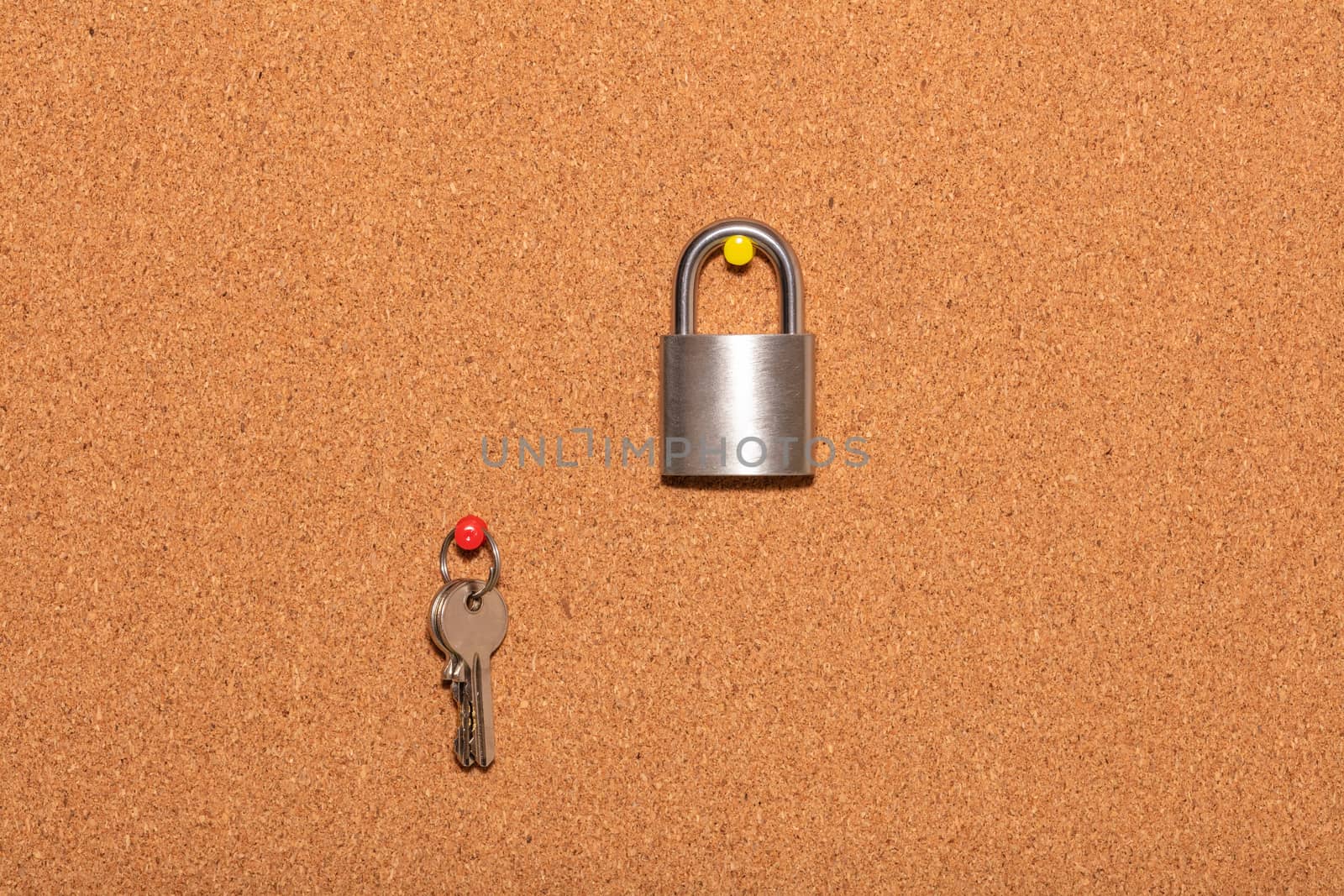 Closed padlock with keys hanging on a separate pin on an empty corkwood notice board in business office. Safety and security reminder, business closure, business for sale concepts.