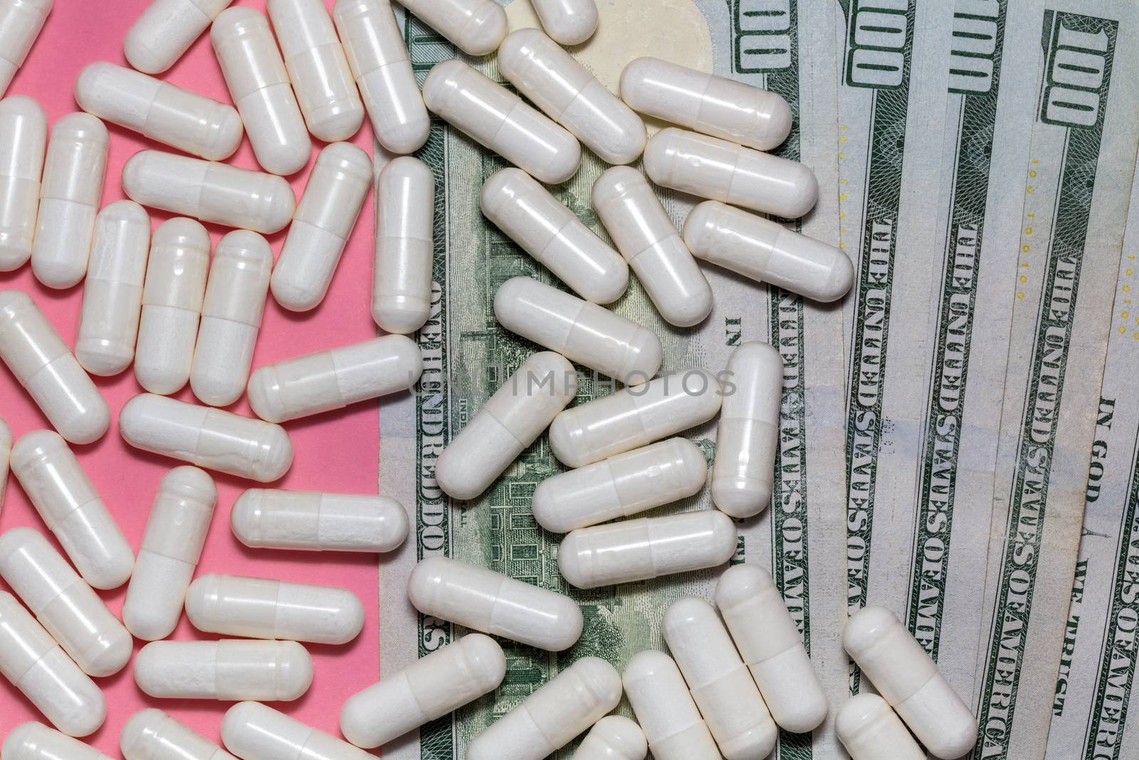 Top close up shot of white pills scattered on top of a few hundreed dollar bills. Pink background. Healthcare, medical, pharmaceutical business, commerce, shopping concepts. New normal concept. by DamantisZ
