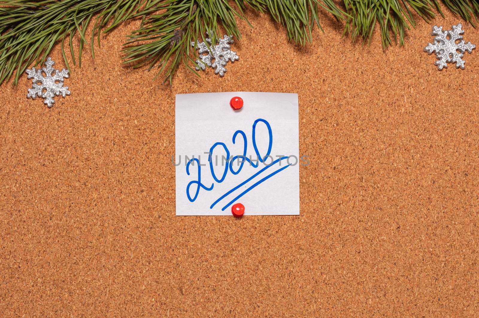 White sticky note with 2020 handwritten on it pinned on notice board which is decorated with pine twigs and snowflakes. 2020 Christmas, new years celebration season concept. Close-up shot.