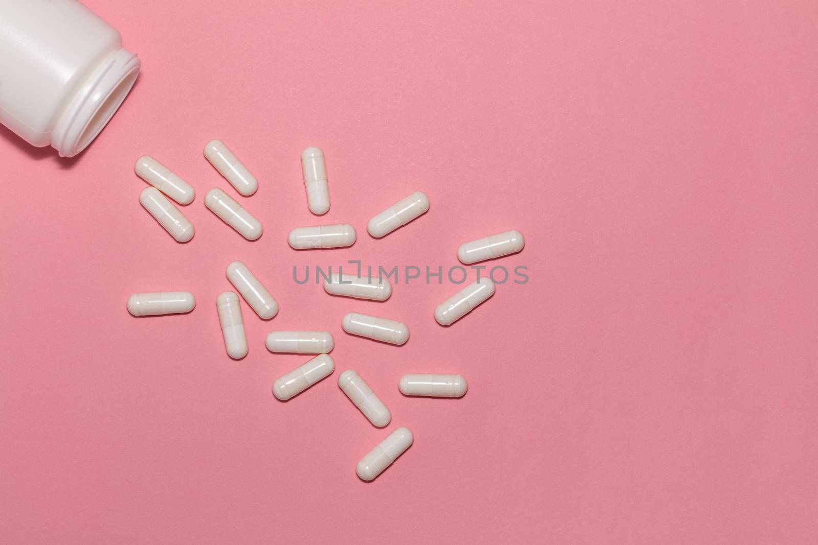 Top view of scattered prescription white pills and a container on pink background with copy space. Healthcare, medical and pharmaceutical concept. by DamantisZ