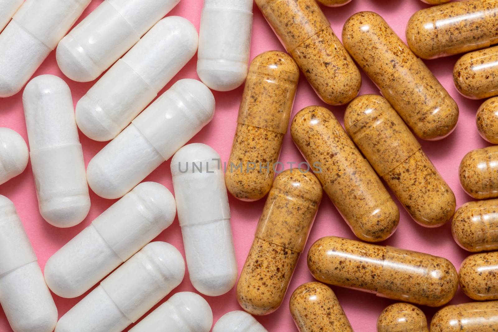 Top close up shot of white and brown pills on pink background. Healthcare, medical and pharmaceutical concept.