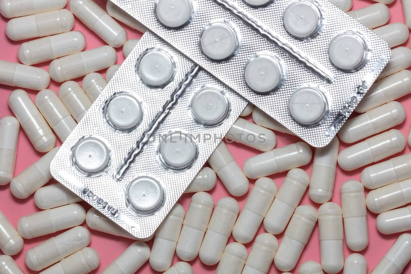 Top close up shot of various white pills on pink background. Healthcare, medical and pharmaceutical concept.