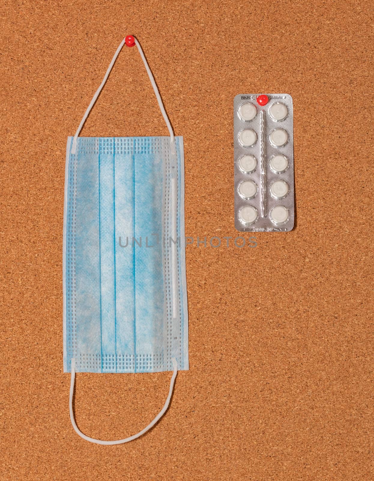 Medical mask and white pills pinned on a corkwood notice board. Healthcare concept. by DamantisZ