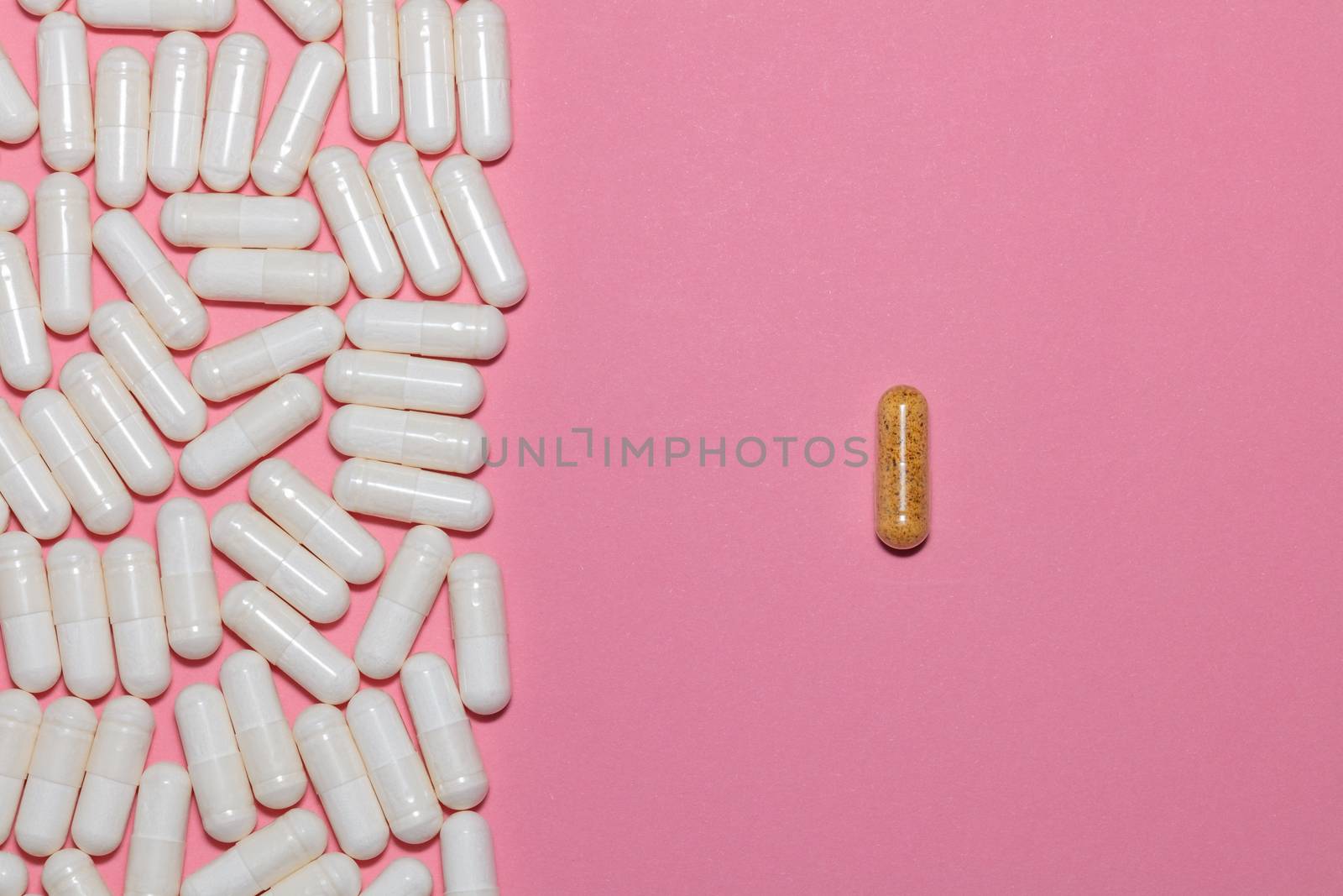 Top view of white pills on one side and a single brown pill on the other side on pink background with copy space. Healthcare, medical and pharmaceutical concept.