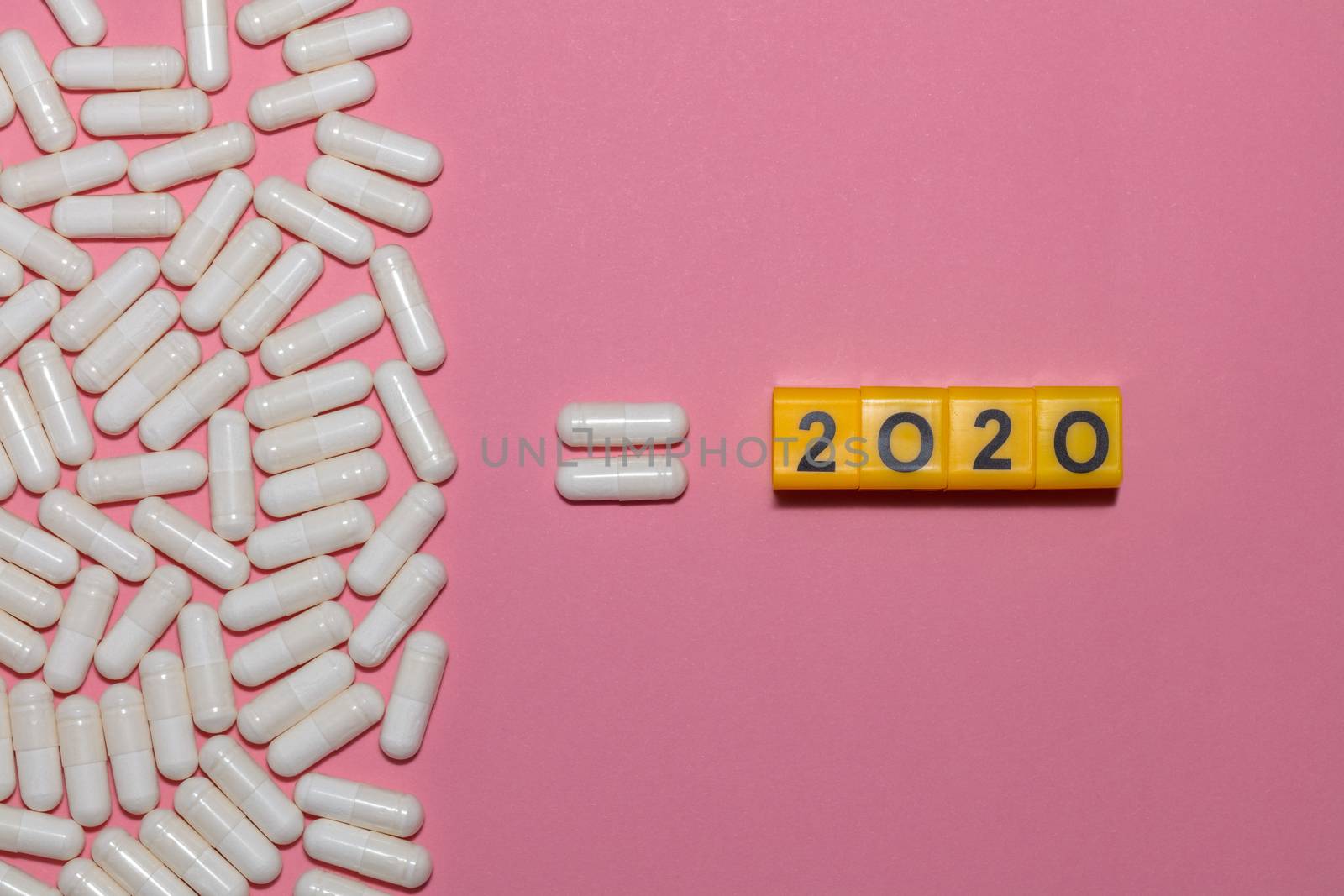Top view of white pills equal 2020 on pink background with copy space. 2020 is formed from yellow cubes with black digits. Healthcare concept. New normal and reality concept.