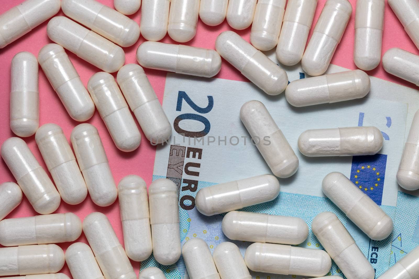 Top close up shot of white pills scattered on top of a few euro bills. Pink background. Healthcare, medical, pharmaceutical business, commerce, shopping concepts. New normal concept.