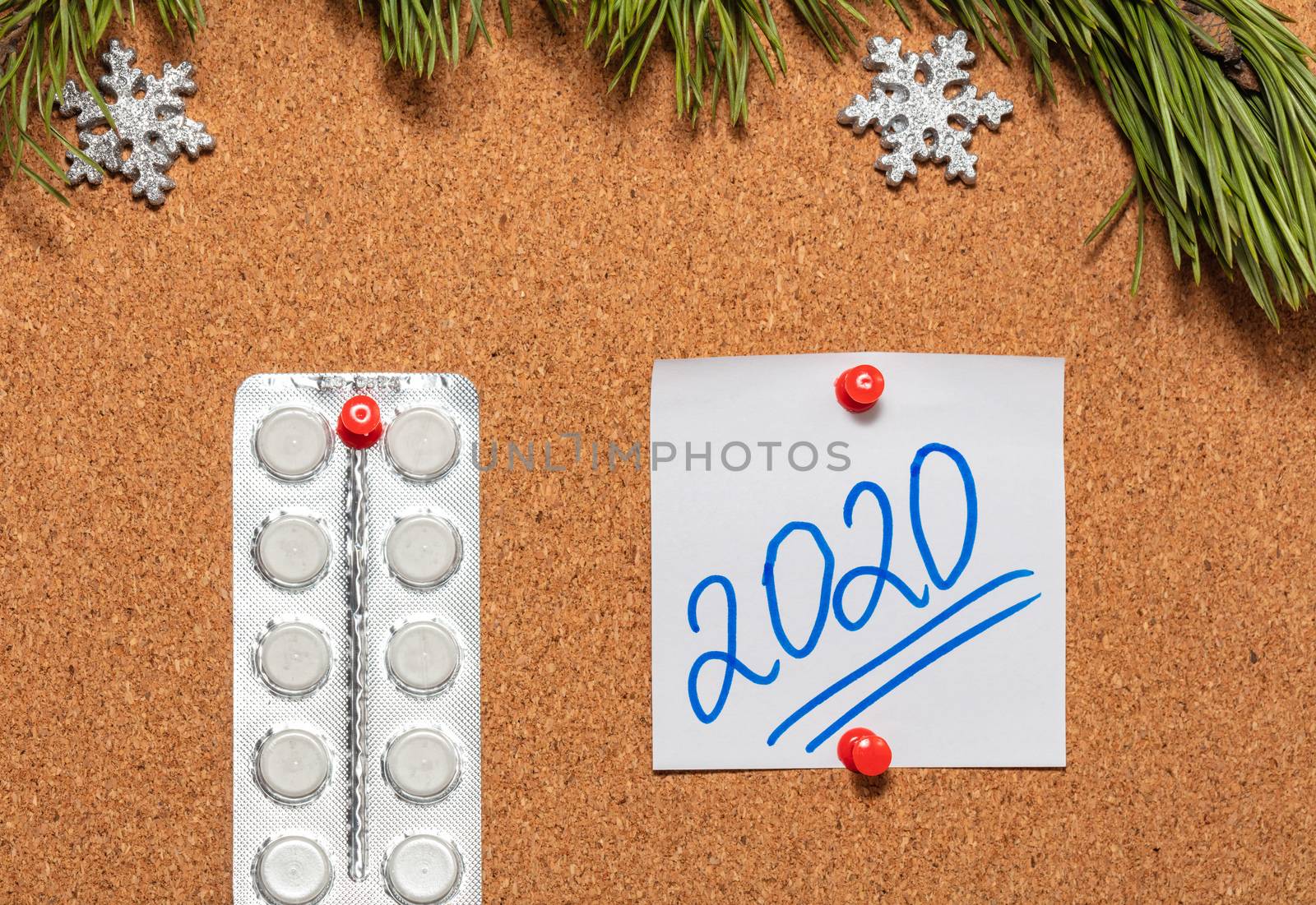 White pills, white sticky note with 2020 pinned on notice board which is decorated with pine twigs and snowflakes at the top. Healthcare, christmas, new years celebration, new normal concepts.