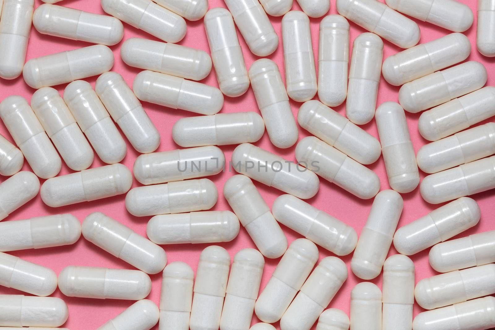 Top close up shot of white pills on pink background. Healthcare, medical and pharmaceutical concept. by DamantisZ