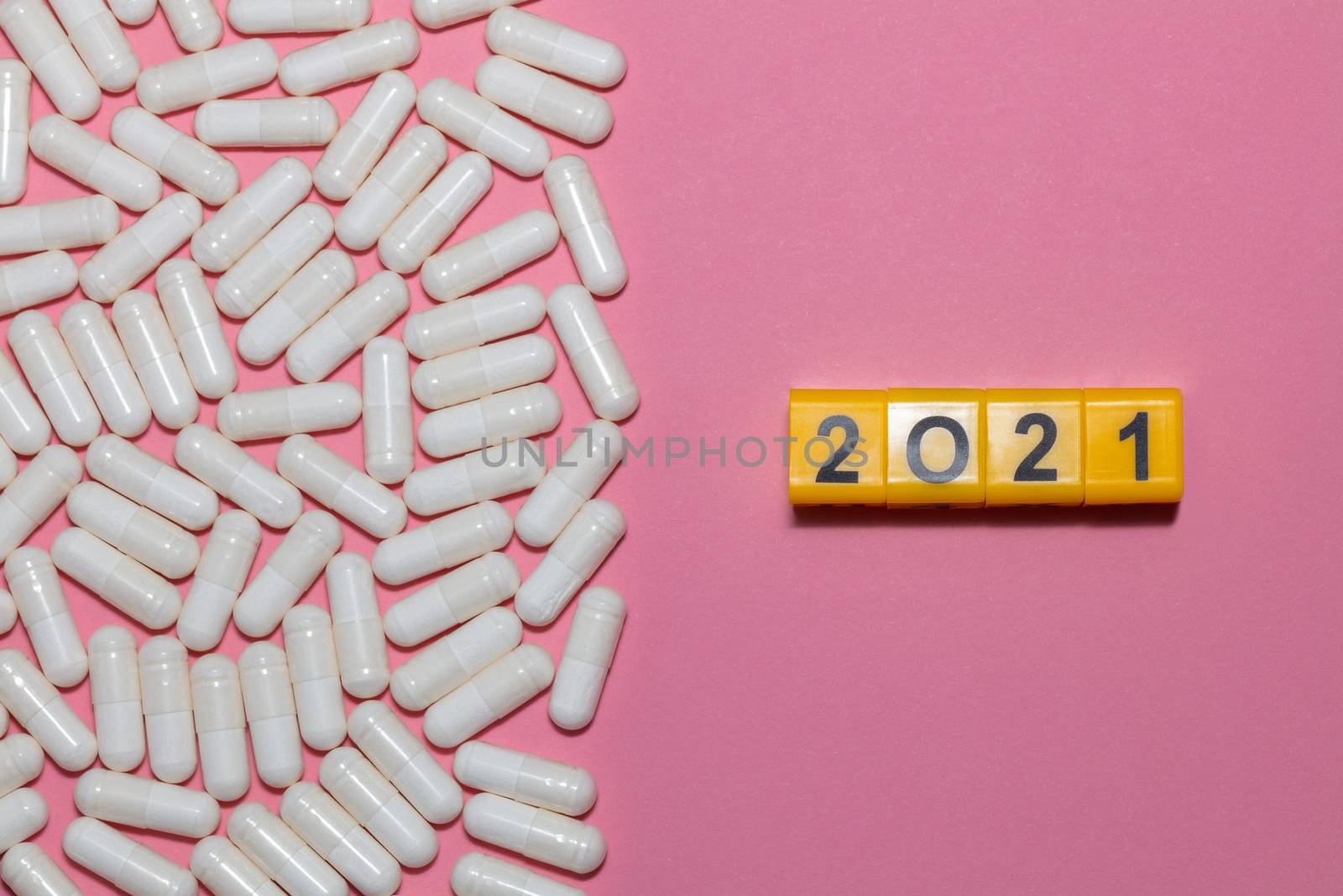Top view of white pills on pink background with copy space. Yellow cubes with black digits form 2021 next to the pills. Healthcare, medical and pharmaceutical concept. New normal and reality concept.