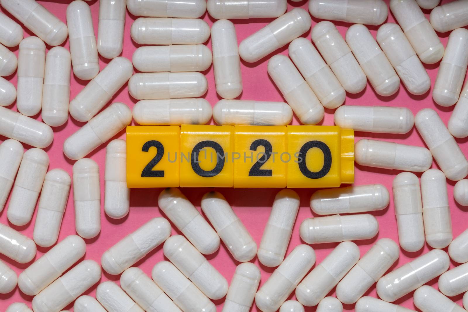 Top close up shot of white pills surrounding yellow cubes with black digits which form 2020 year. Pink background. Healthcare, medical and pharmaceutical concept. New normal and reality concept
