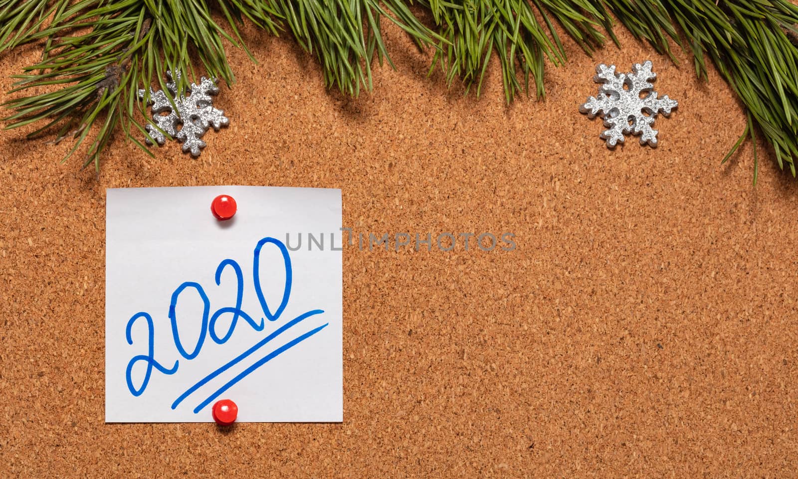 White sticky note with 2020 handwritten on it pinned on notice board which is decorated with pine twigs and snowflakes. 2020 Christmas, new years celebration season concept. Close-up shot. Copy space by DamantisZ