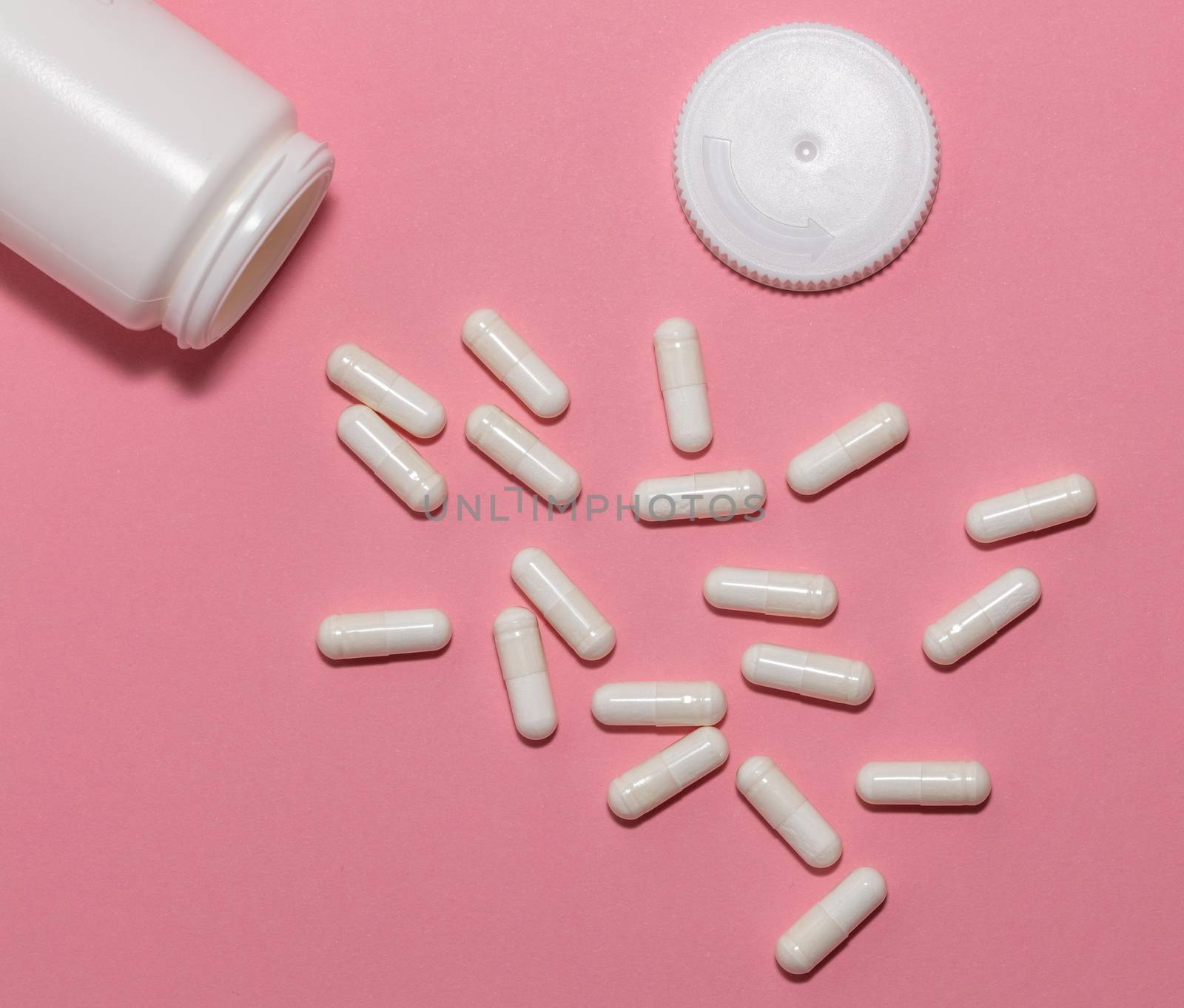 Top view of scattered prescription white pills, container, cap on pink background. White container and white pills scattered on pastel pink background. Healthcare, medical and pharmaceutical concept.