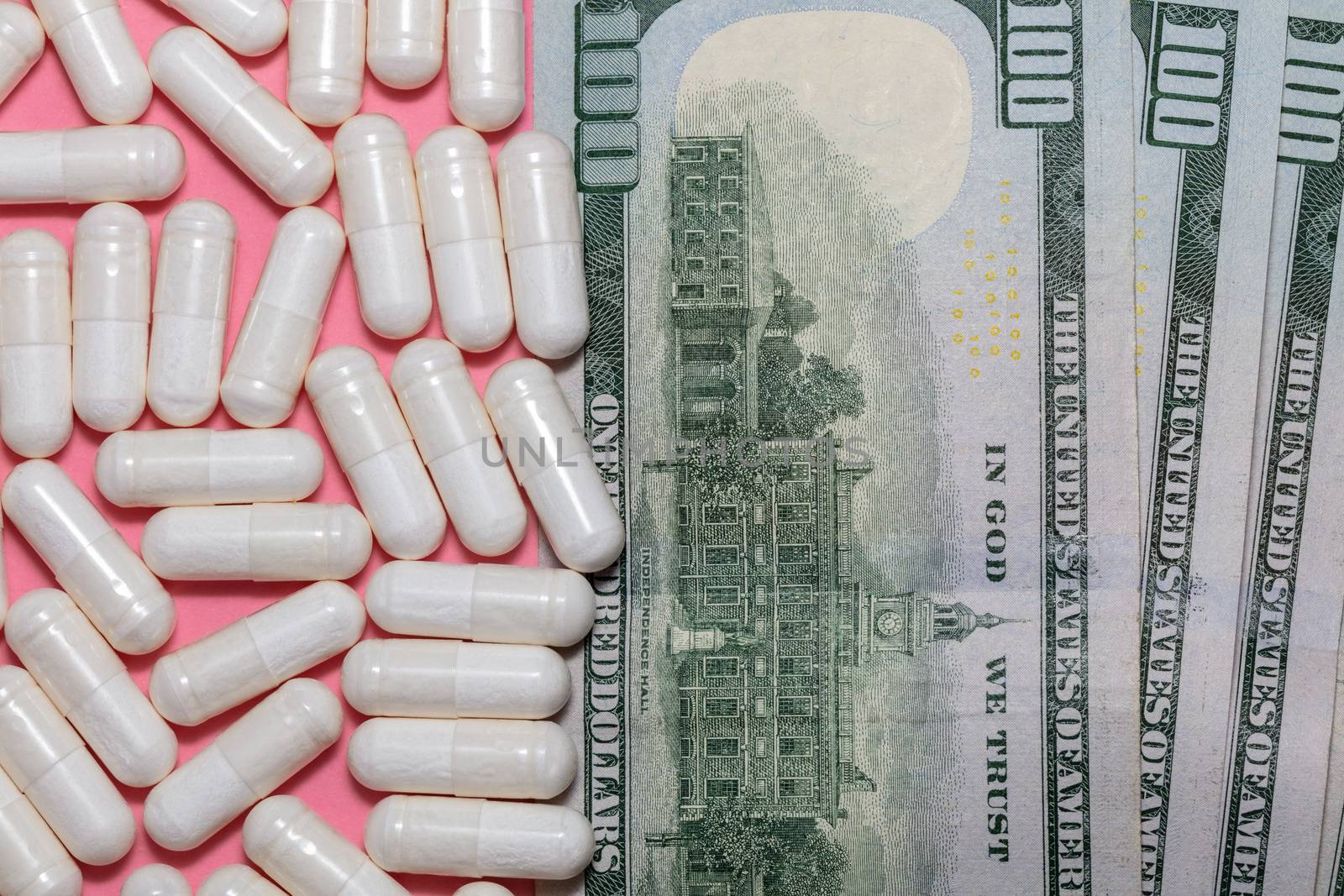 Top close up shot of white pills and a few hundreed dollar bills next to them on pink background. Healthcare, medical, pharmaceutical business, commerce, shopping concepts. New normal concept.