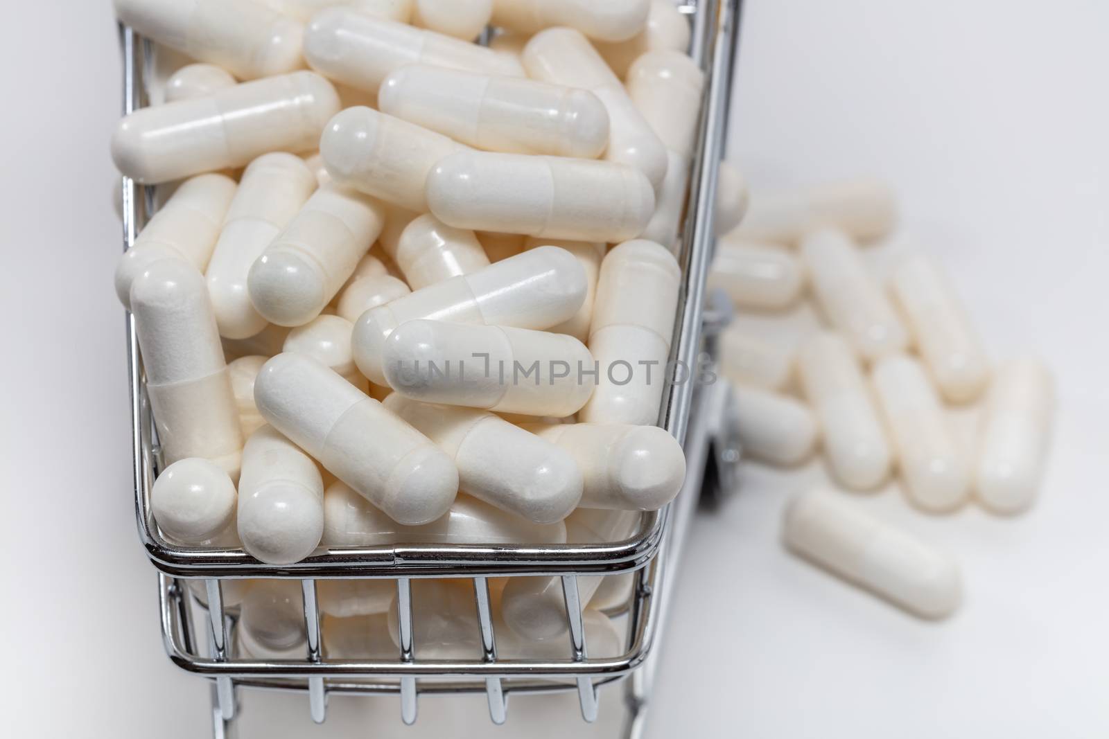 High angle shot of a small shopping cart full of white pills. White background. Close up shot. Some pills under the cart blurry in the background. Shopping online, pharmaceutical business concepts.