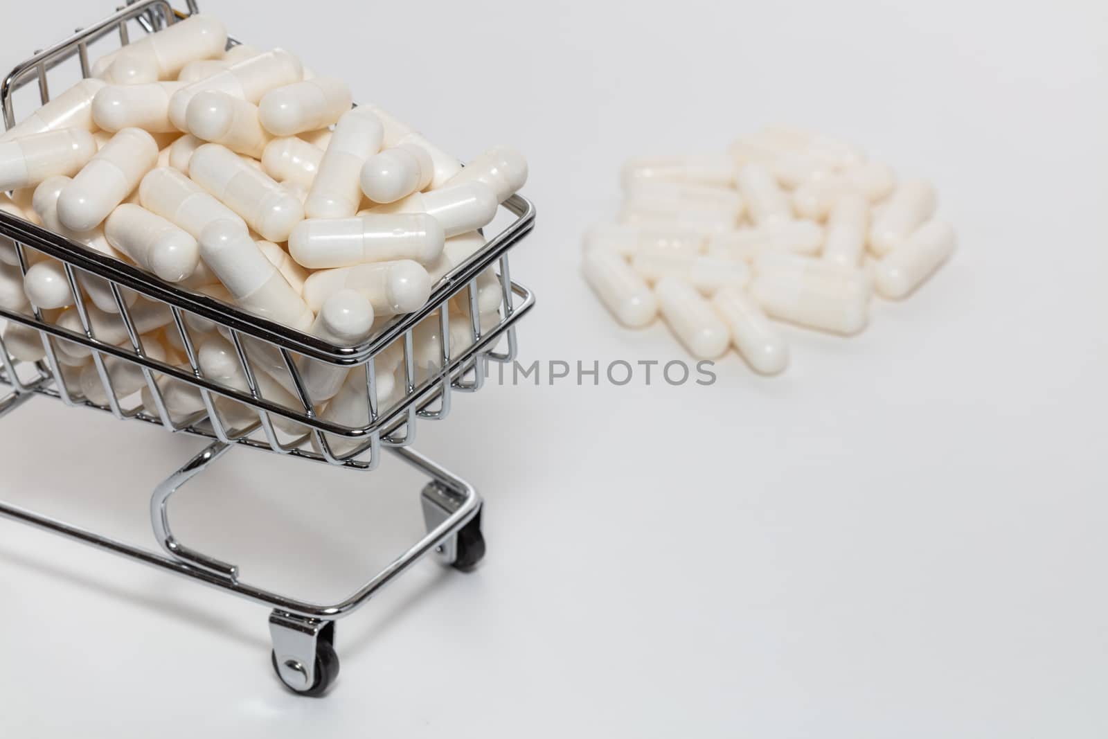High angle shot of small shopping cart full of white pills. Bunch of pills blurry in the background. White background, close up shot. Shopping online, buying medicine, pharmaceutical business concepts