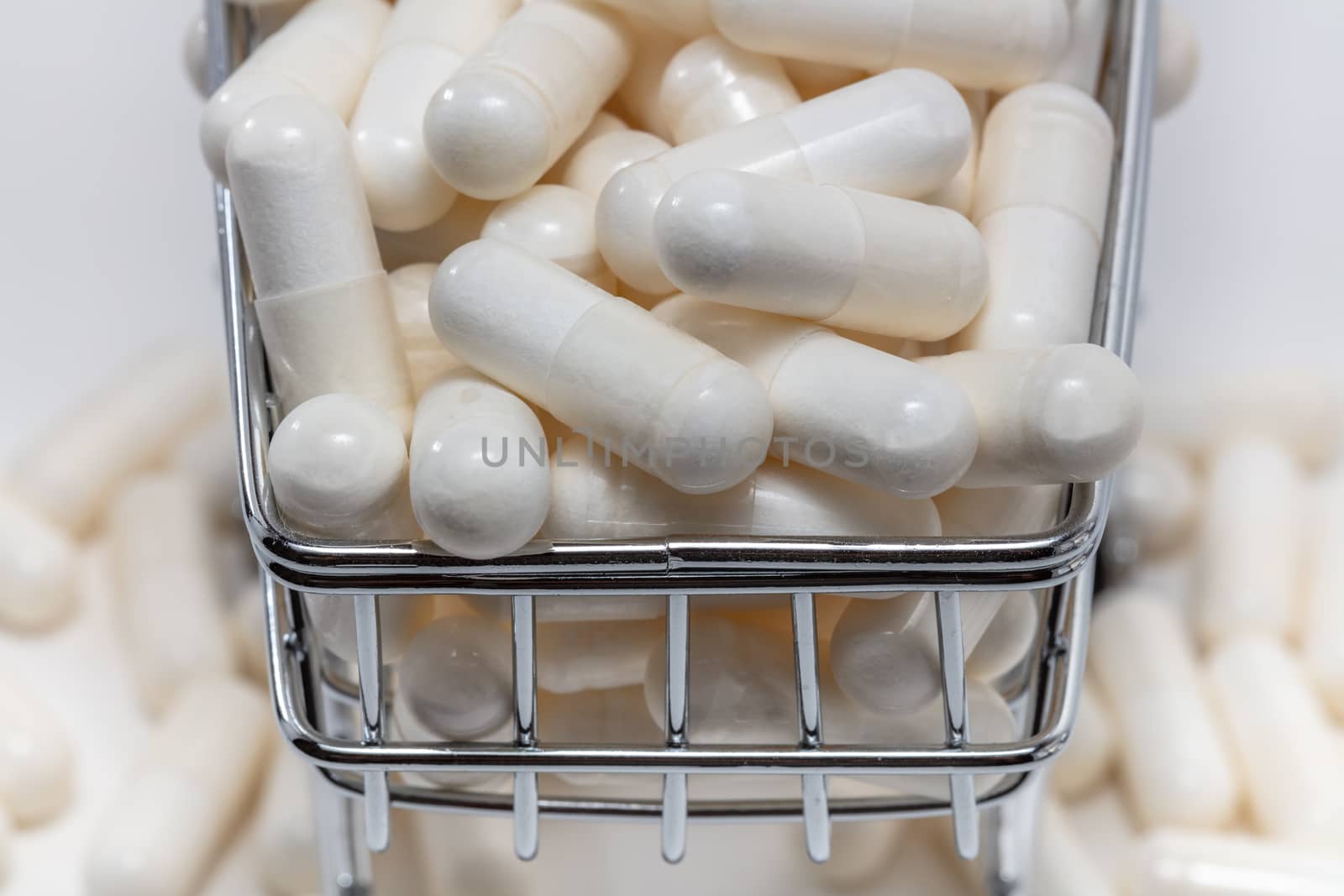 High angle shot of a small shopping cart full of white pills. White background. Close up shot. Some pills under the cart blurry in the background. Shopping online, pharmaceutical business concepts.