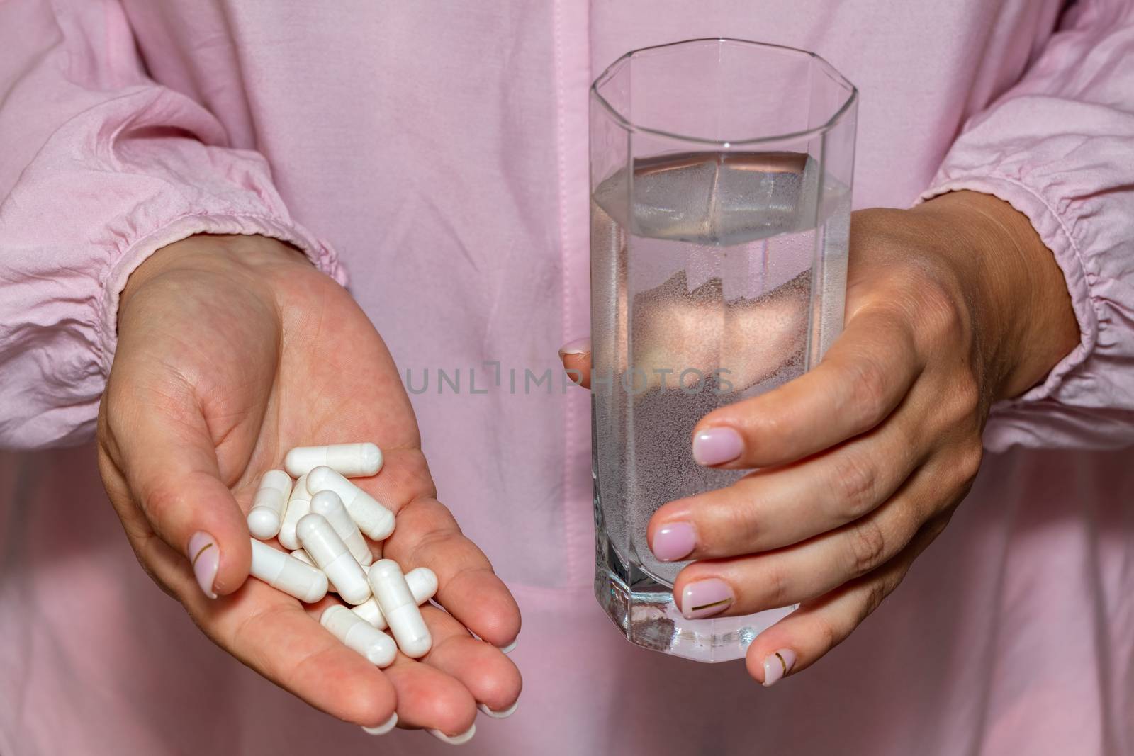 High angle closeup shot of female hands holding a bunch of white pills and a glass of water. Healthcare, medical and pharmaceutical concept. by DamantisZ