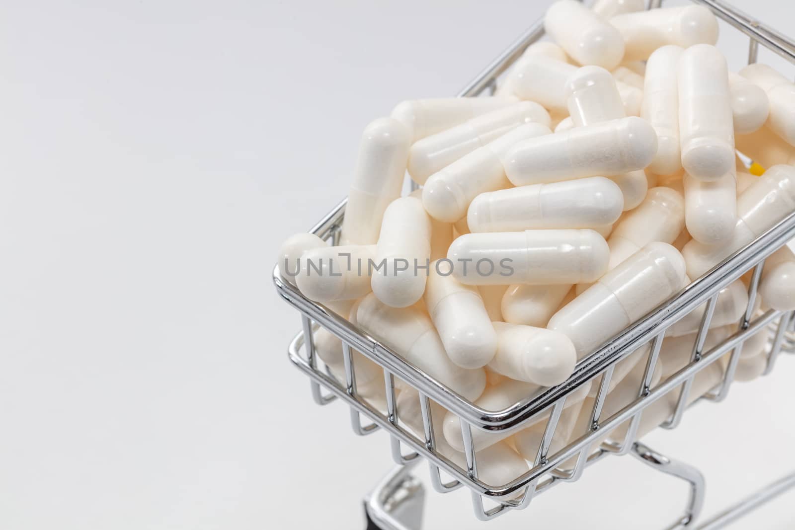 High angle shot of a small shopping cart full of white pills. White background, copy space. Close up shot. Shopping online, buying medicine, pharmaceutical business concepts.