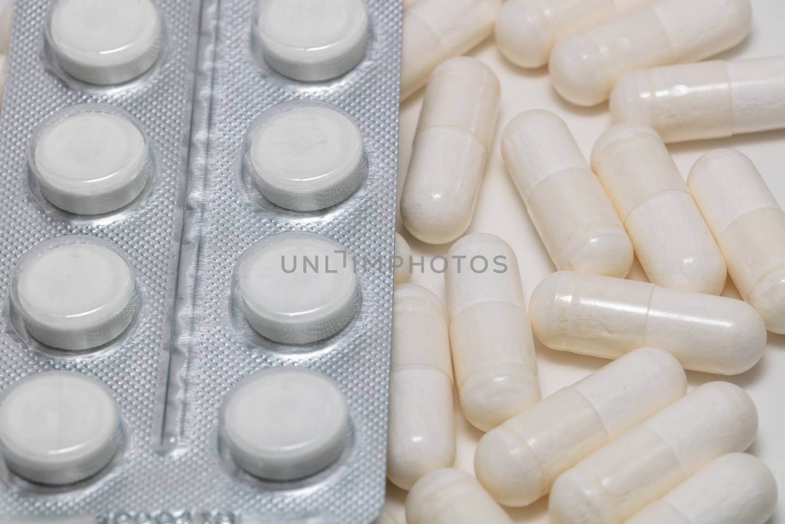 High angle close up shot of various white pills on white background. Some of them are out of focus. Pharmaceutical business and medicine sale concepts.