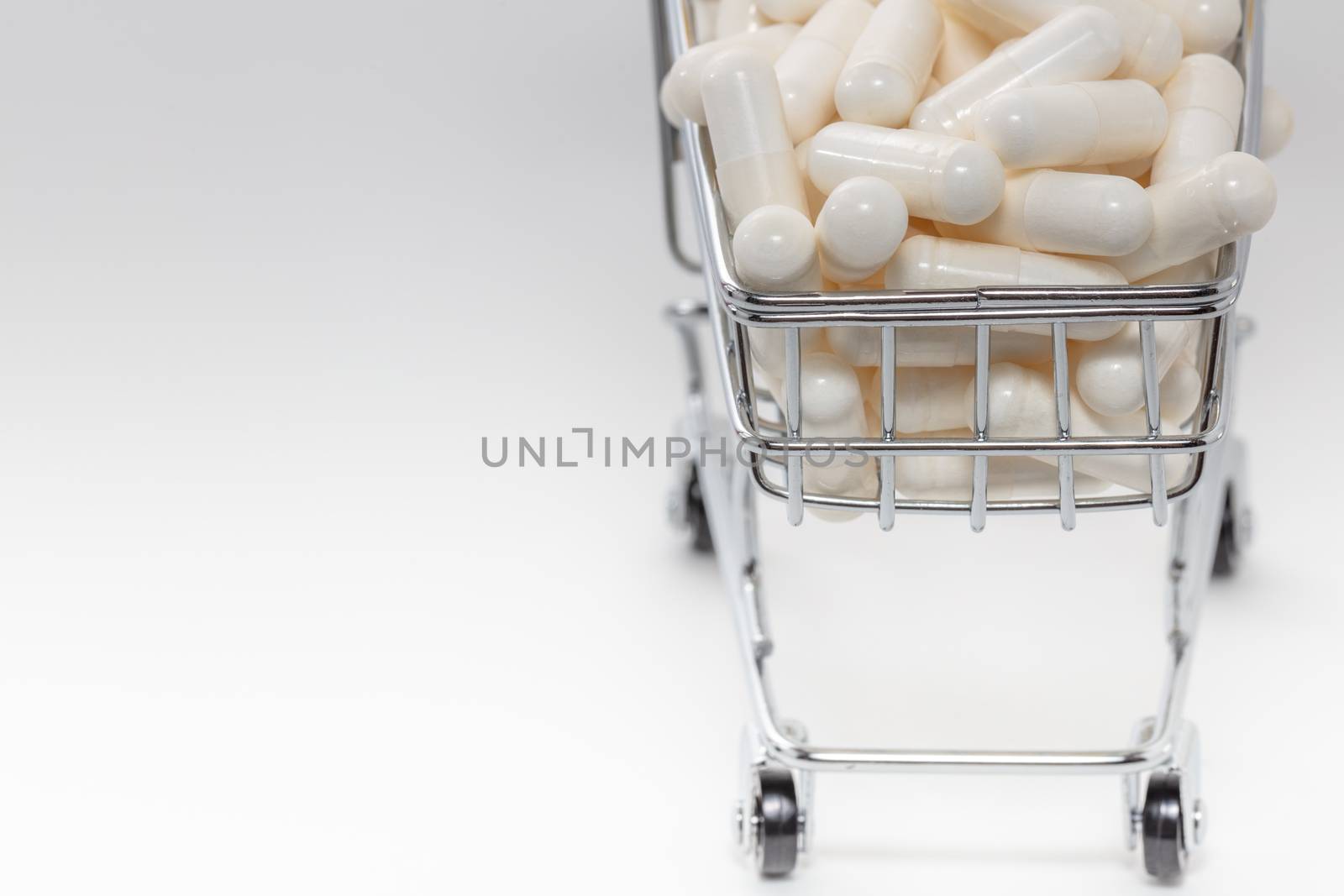 High angle shot of a small shopping cart full of white pills. White background, copy space. Close up shot. Shopping online, buying medicine, pharmaceutical business concepts. by DamantisZ