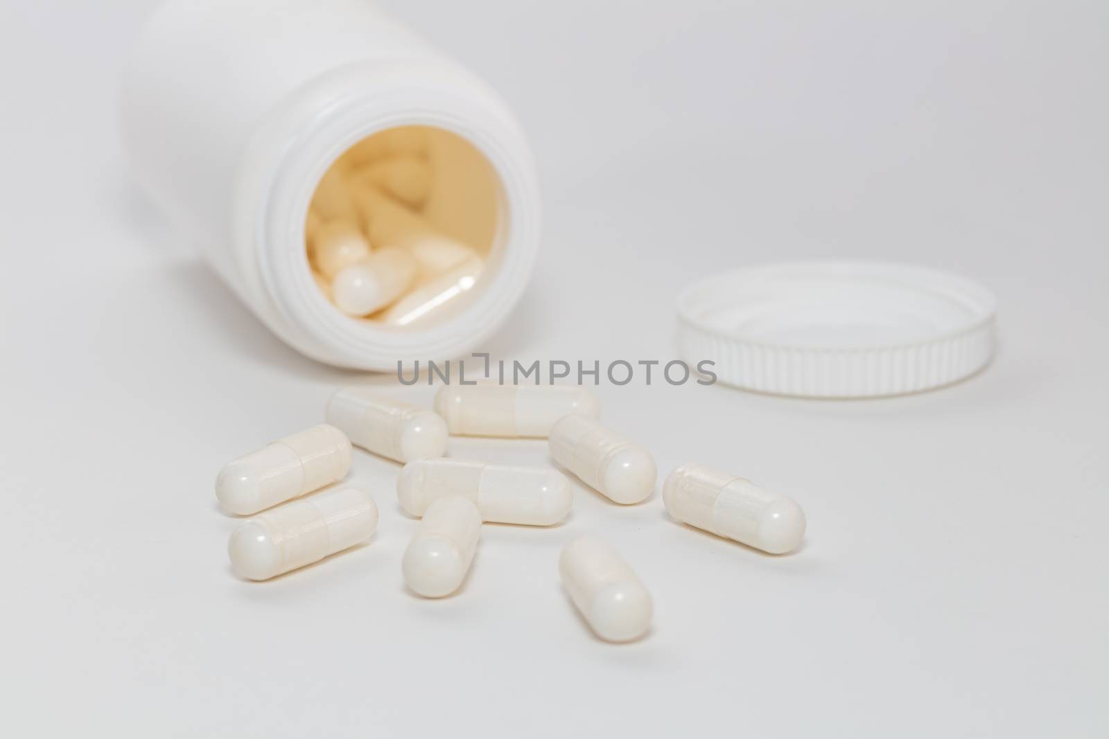 Bunch of white scattered pills on white background. White pills container and cap next to them slightly out of focus in the background. Close up. Pharmaceutical business and medicine sale concepts.