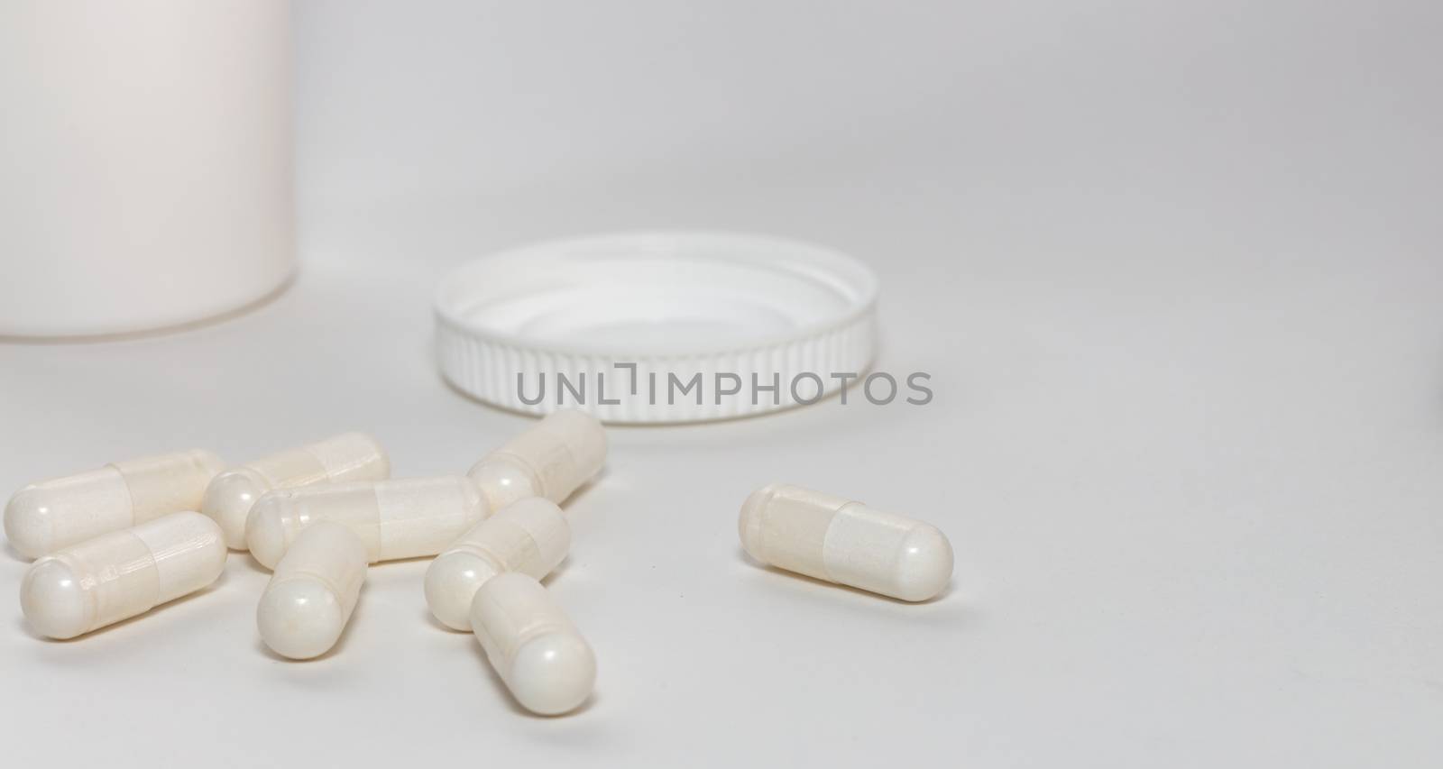 Bunch of white scattered pills on white background. White pills container and cap next to them slightly out of focus in the background. Close up. Pharmaceutical business and medicine sale concepts.