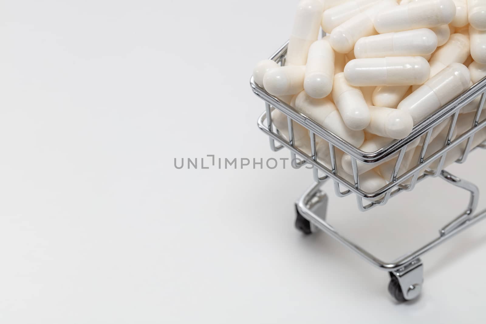 High angle shot of a small shopping cart full of white pills. White background, copy space. Close up shot. Shopping online, buying medicine, pharmaceutical business concepts. by DamantisZ