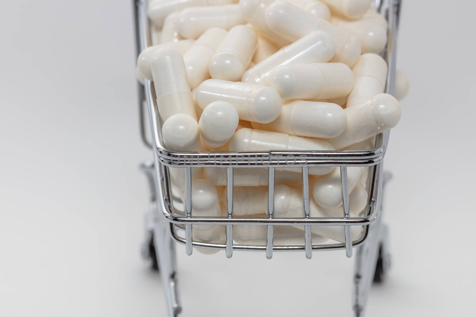 High angle shot of a small shopping cart full of white pills. White background. Close up shot. Shopping online, buying medicine, pharmaceutical business concepts.