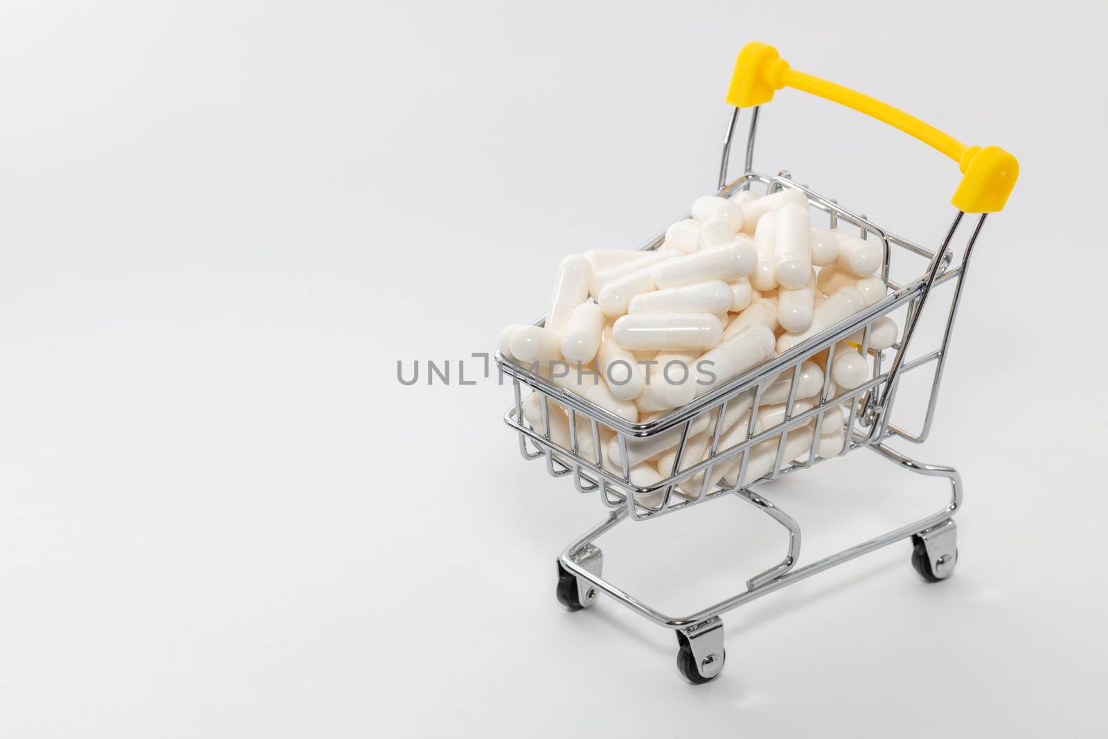 High angle shot of a small shopping cart full of white pills. White background, copy space. Shopping online, buying medicine, pharmaceutical business concepts.