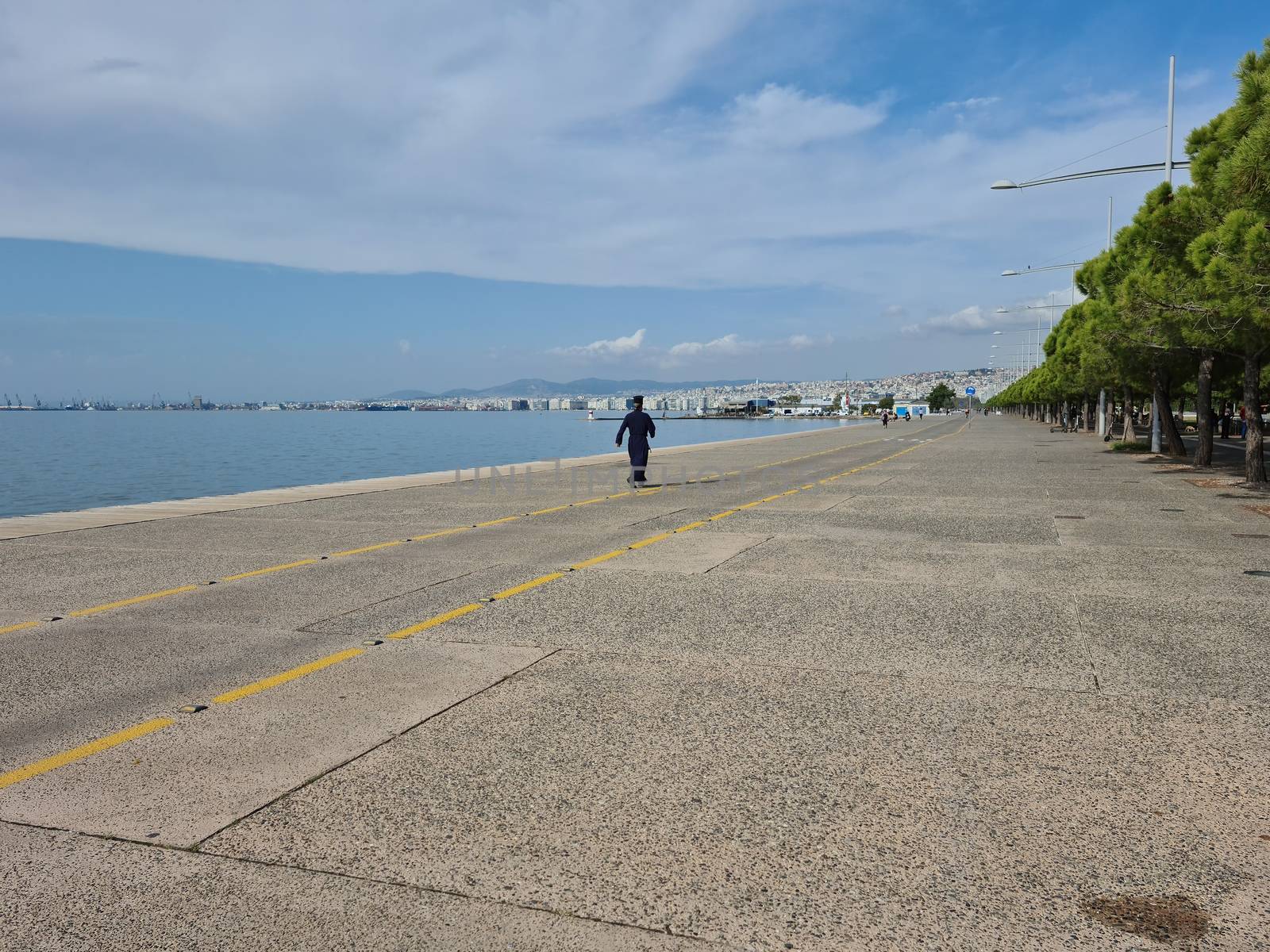 Day view of a Greek clergyman in clerical clothing at the pedestrian area of the city waterfront.