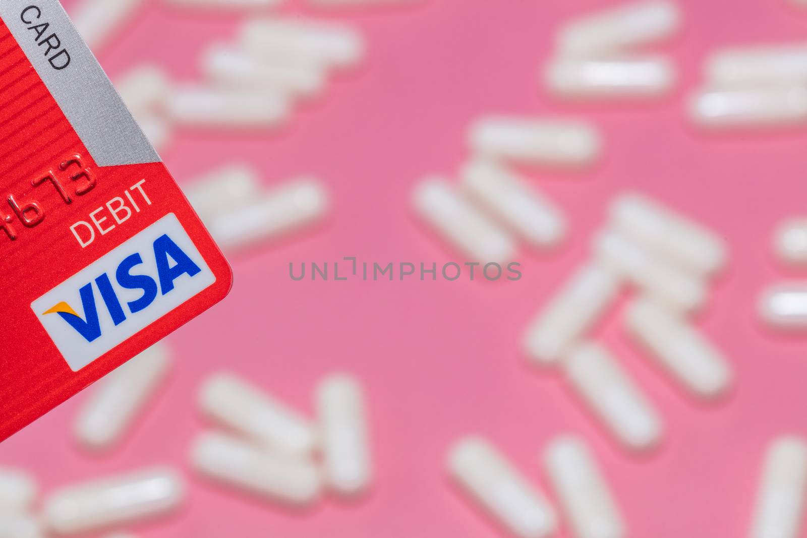 Barnaul, Russia - October 13, 2020: Shot of a corner of a red visa debit card and white pills out of focus on pink background. Healthcare, pharmaceutical business, commerce, shopping concepts.