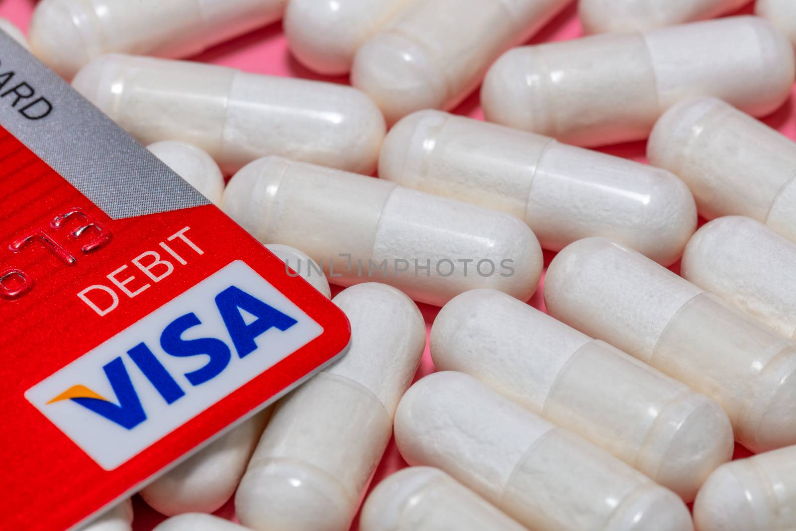 Barnaul, Russia - October 13, 2020: High angle close up shot of corner of a red visa debit card, white pills on pink background. Close up shot. Healthcare, pharmaceutical business, commerce concepts