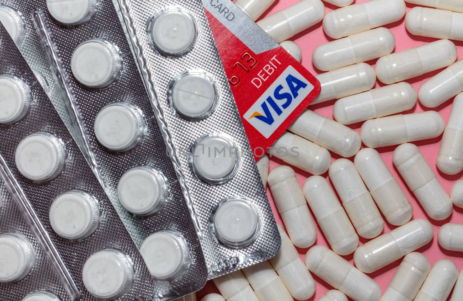 Barnaul, Russia - October 13, 2020: Top angle shot of various white pills and a visa debit card on pink background. Pharmaceutical business, commerce, shopping for medical supplies concepts.