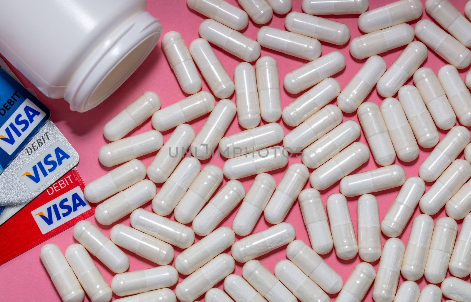 Barnaul, Russia - October 13, 2020: Top angle shot of white pills, three visa debit cards, and a white container on pink background. Container out of focus. Pharmaceutical business, shopping concepts