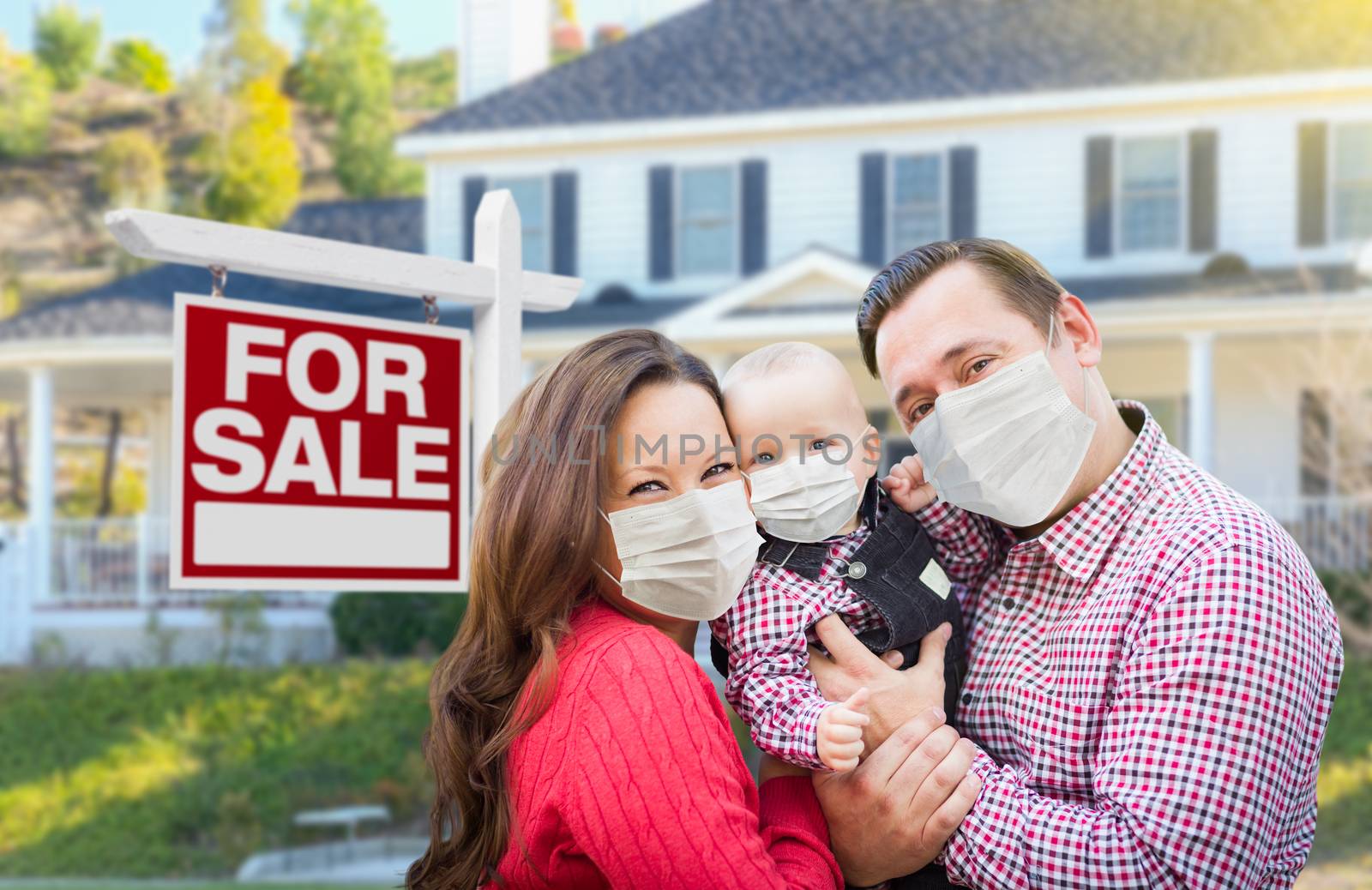 Happy Young Family Wearing Medical Face Masks In Front of New House and Sold For Sale Sign.