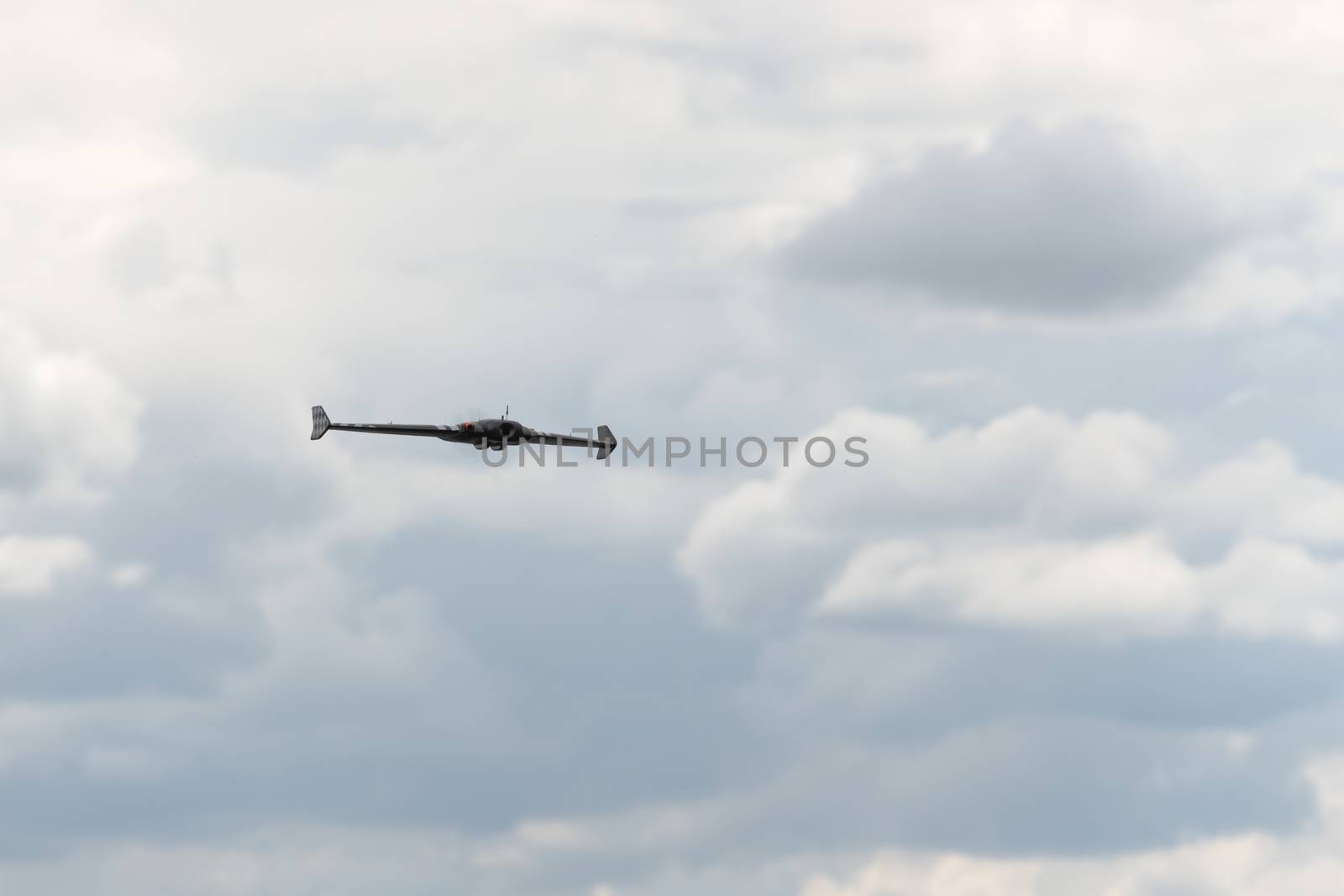 Gentle fluffy clouds in a grey sky form the background behind this FPV first person view flying wing drone. Selective focus and head on view.