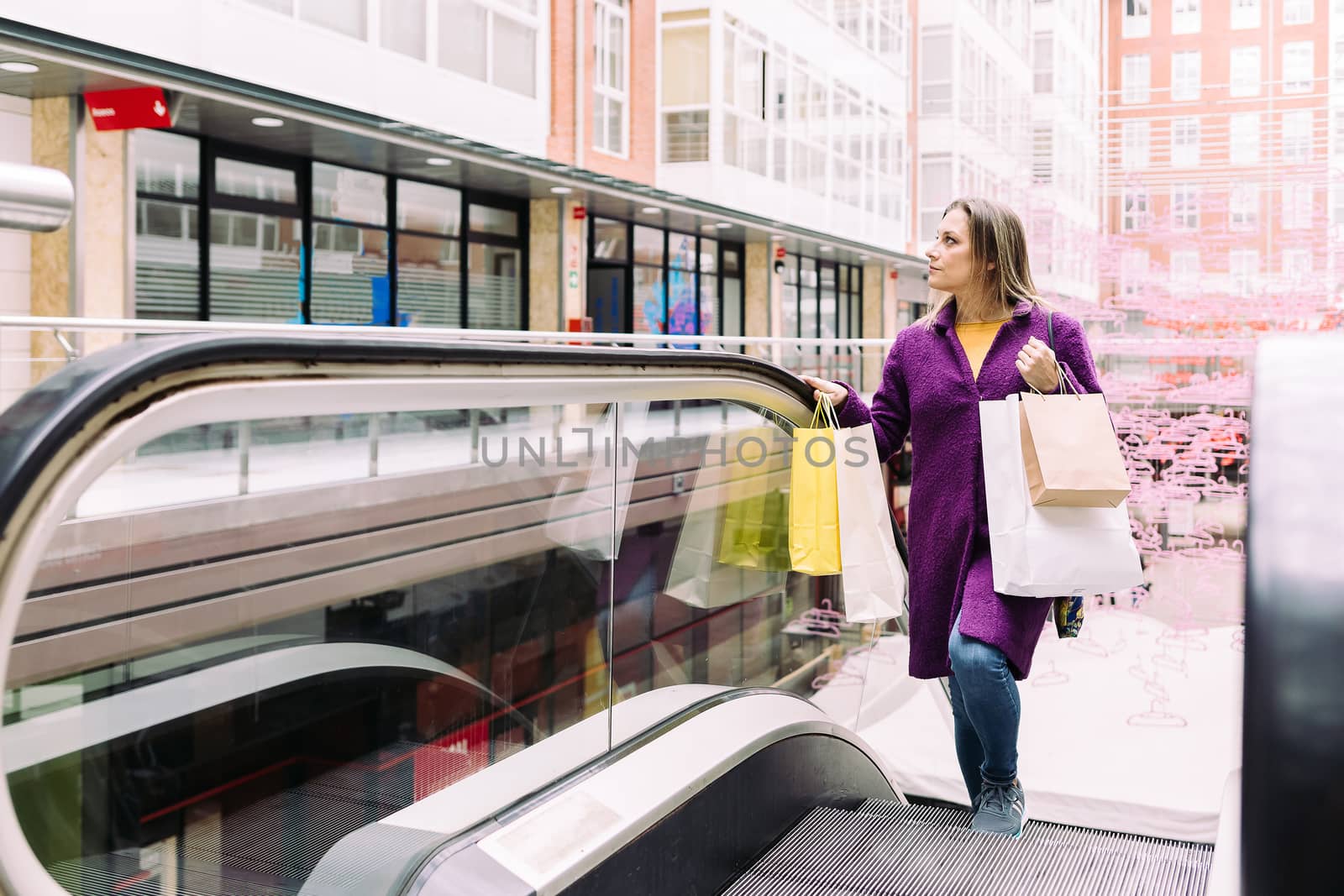 Woman on an escalator with shopping bags in her hands by JRPazos