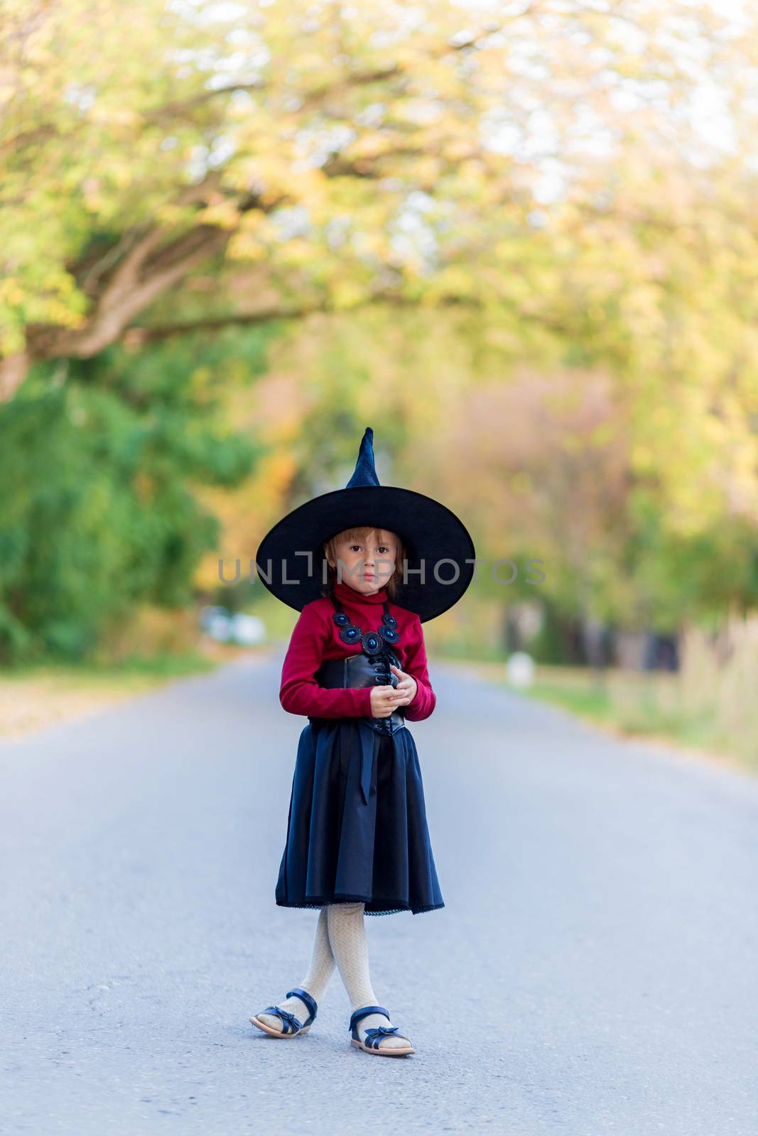 Little girl in a witch costume stands on the road on a halloween party in the village