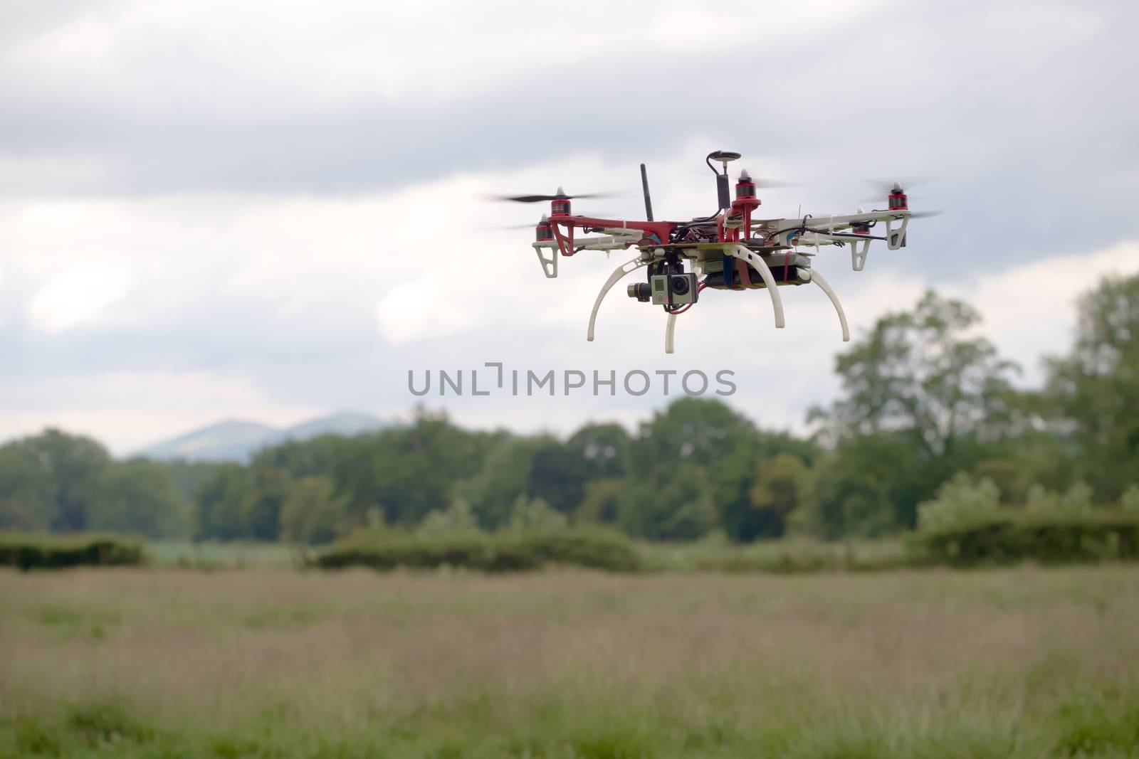 Large hex copter camera drone hovers in front of a rural back ground of the malvern hills. Autonomous FPV modern flight, gimbal stabilized camera