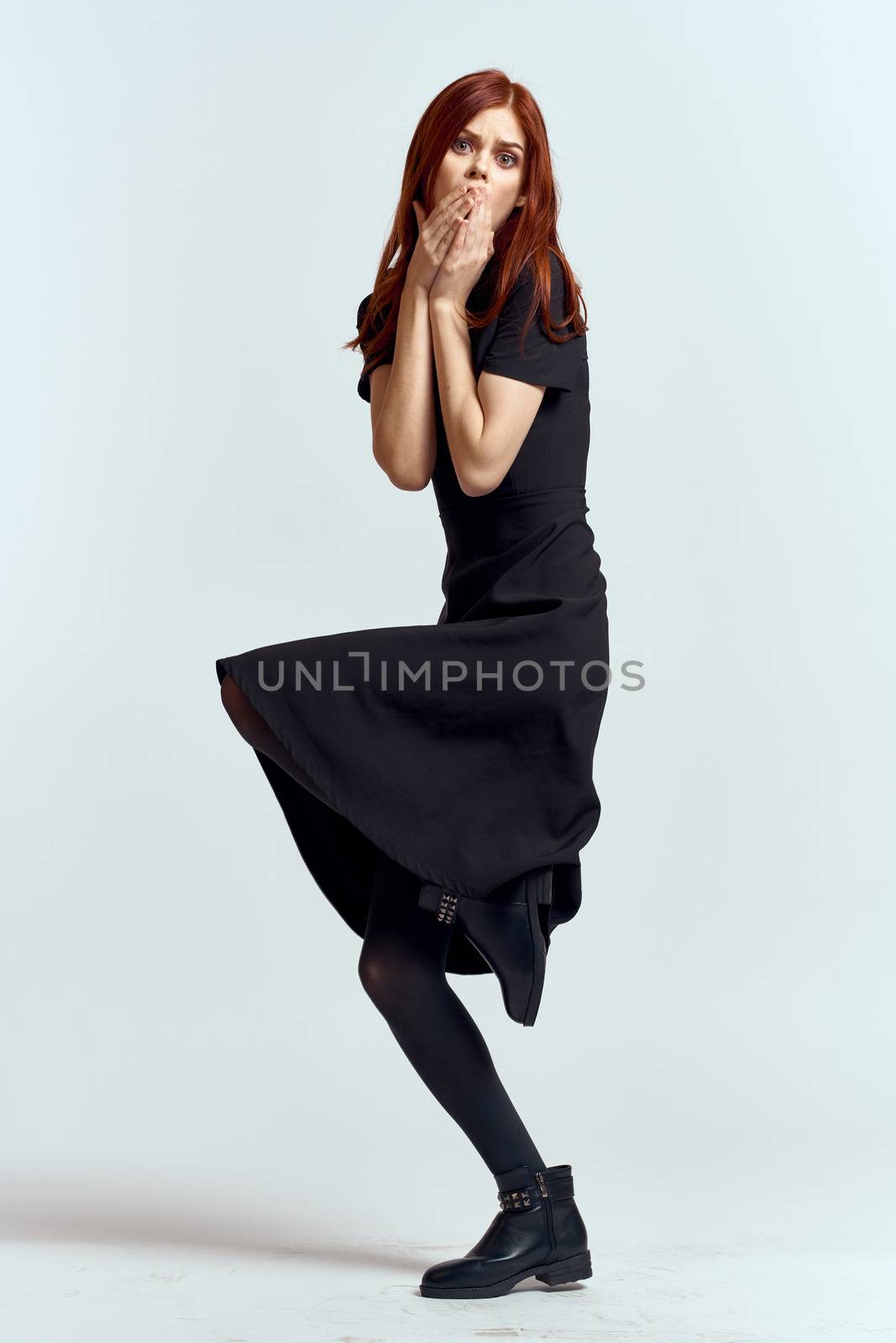 A woman in a black dress on a light background and pantyhose shoes red hair and pose in full growth. High quality photo