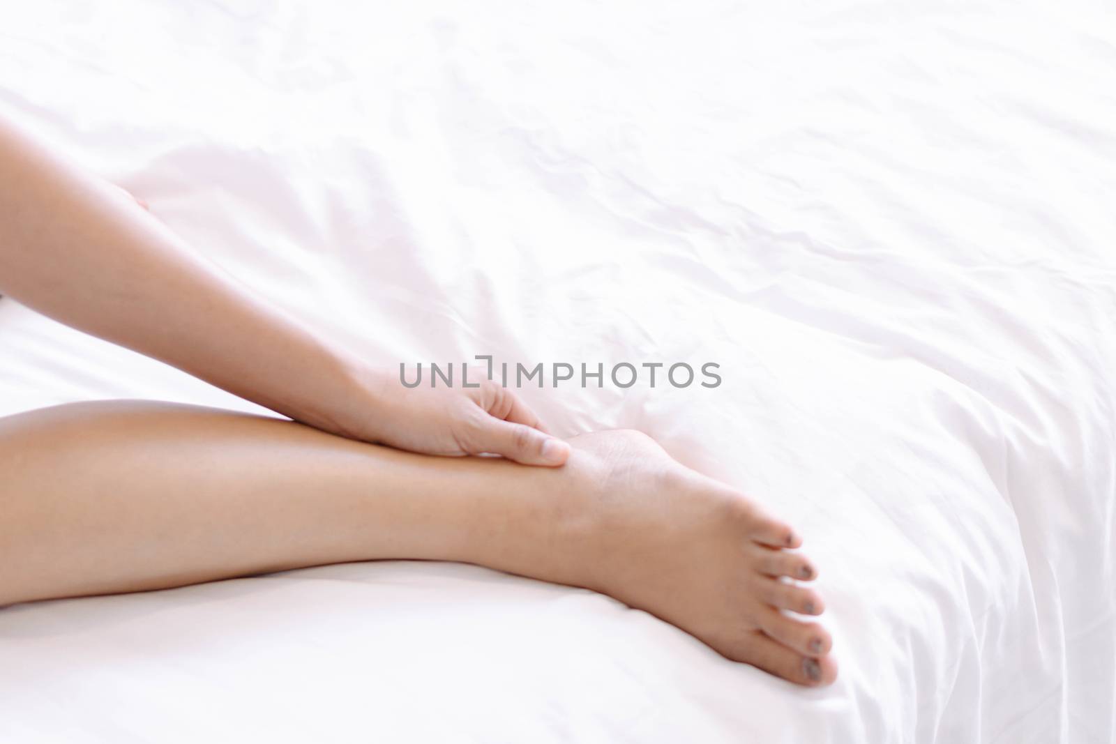 Closeup woman legs on white bed with over light form window, beauty and skin care concept, selective focus